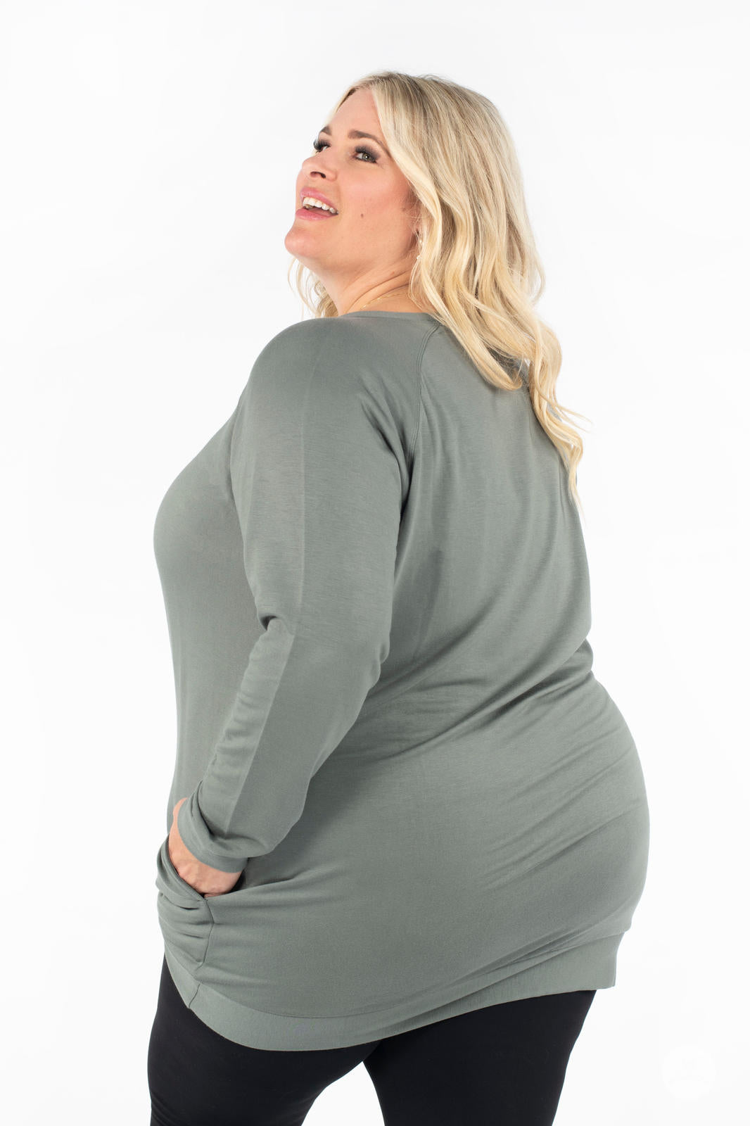 Plus-size model wearing SweetLegs Canada Everyday Raglan Pullover in muted green with hands in pockets facing backward