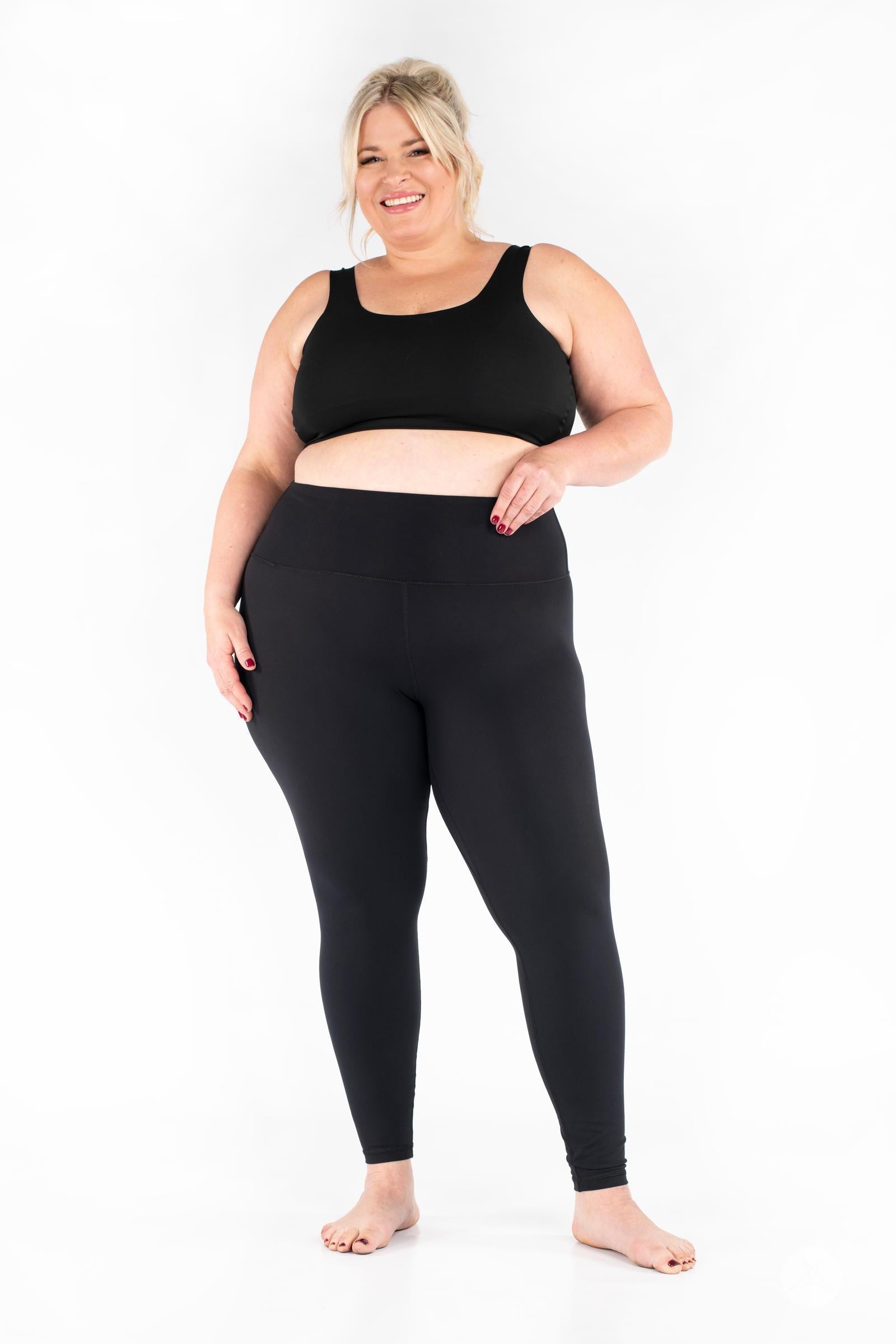 Plus-size model smiling wearing black Free Motion Leggings by SweetLegs Athleisure standing barefoot front view