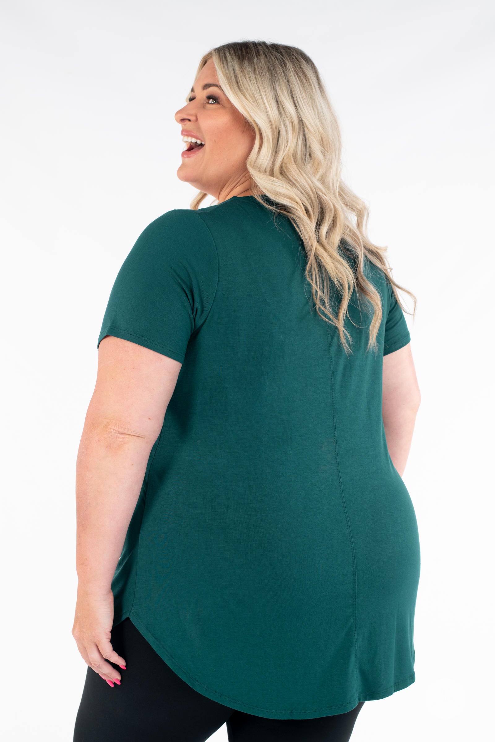 Plus size woman wearing dark green Classic Tee by SweetLegs Canada with high-low hem and short sleeves back view