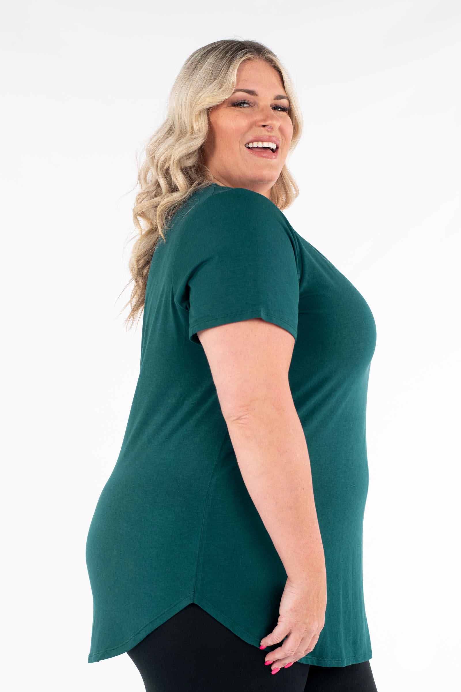 Plus size woman smiling in a dark green Classic Tee by SweetLegs Canada with short sleeves and high-low hem side view