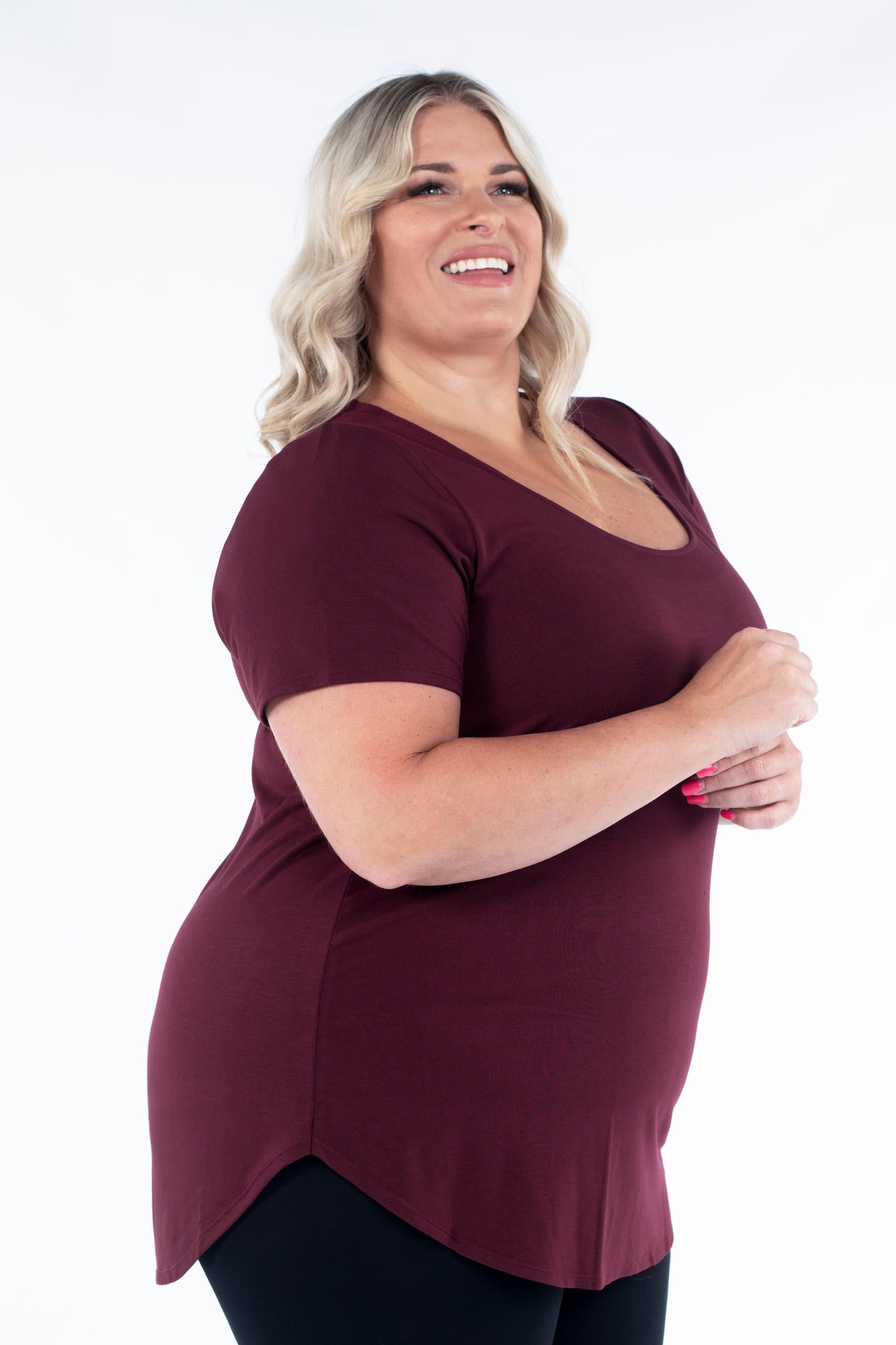 Plus size woman smiling wearing maroon Classic Tee by SweetLegs Canada with scoop neckline and curved hem side view