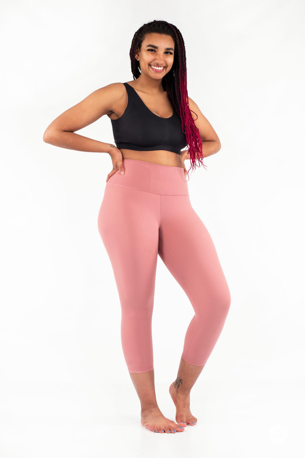 Smiling woman posing barefoot wearing pink Free Motion Crops by Athleisure SweetLegs collection on white background