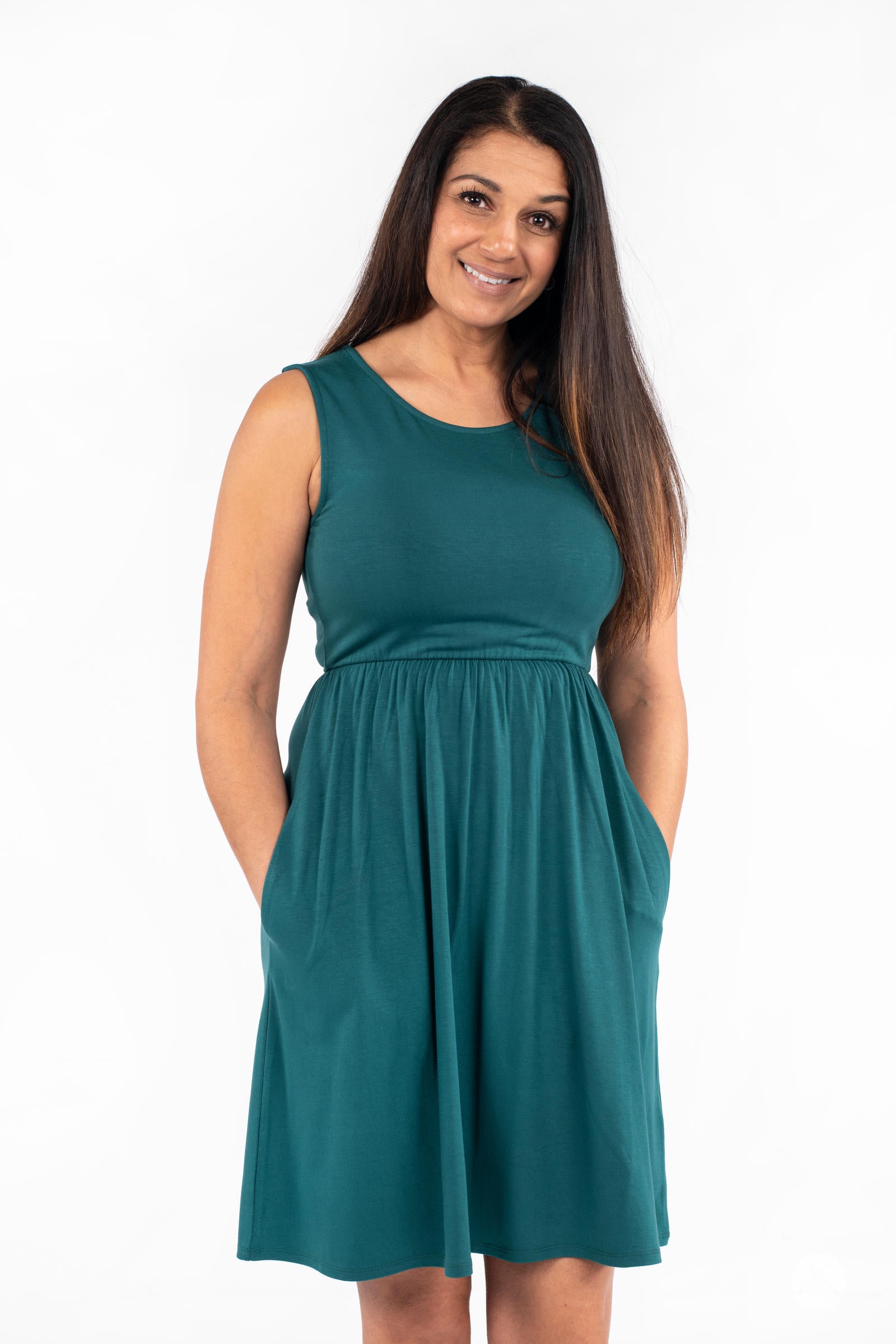 Smiling model wearing SweetTops The Weekender Dress in teal with sleeveless cut and side pockets on white background