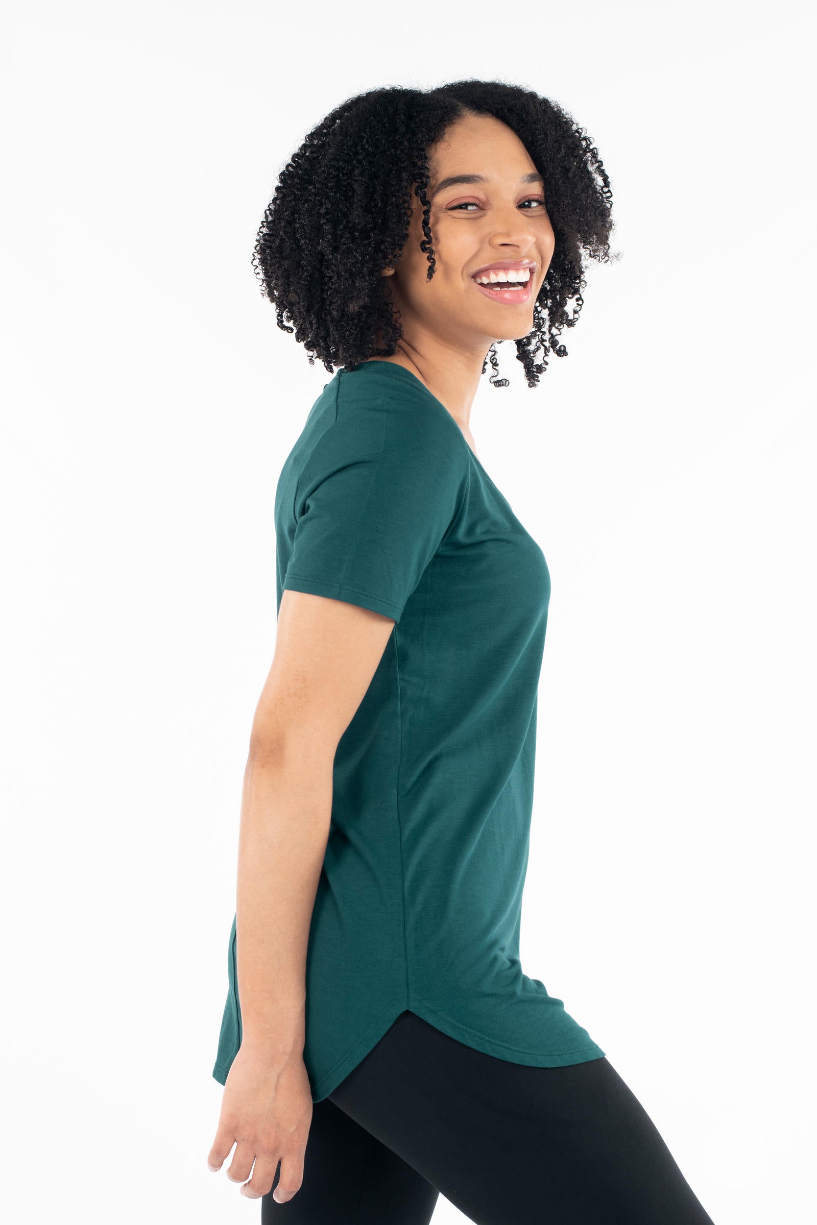 Woman smiling wearing dark green Classic Tee by SweetLegs Canada with short sleeves and side slit hem profile view