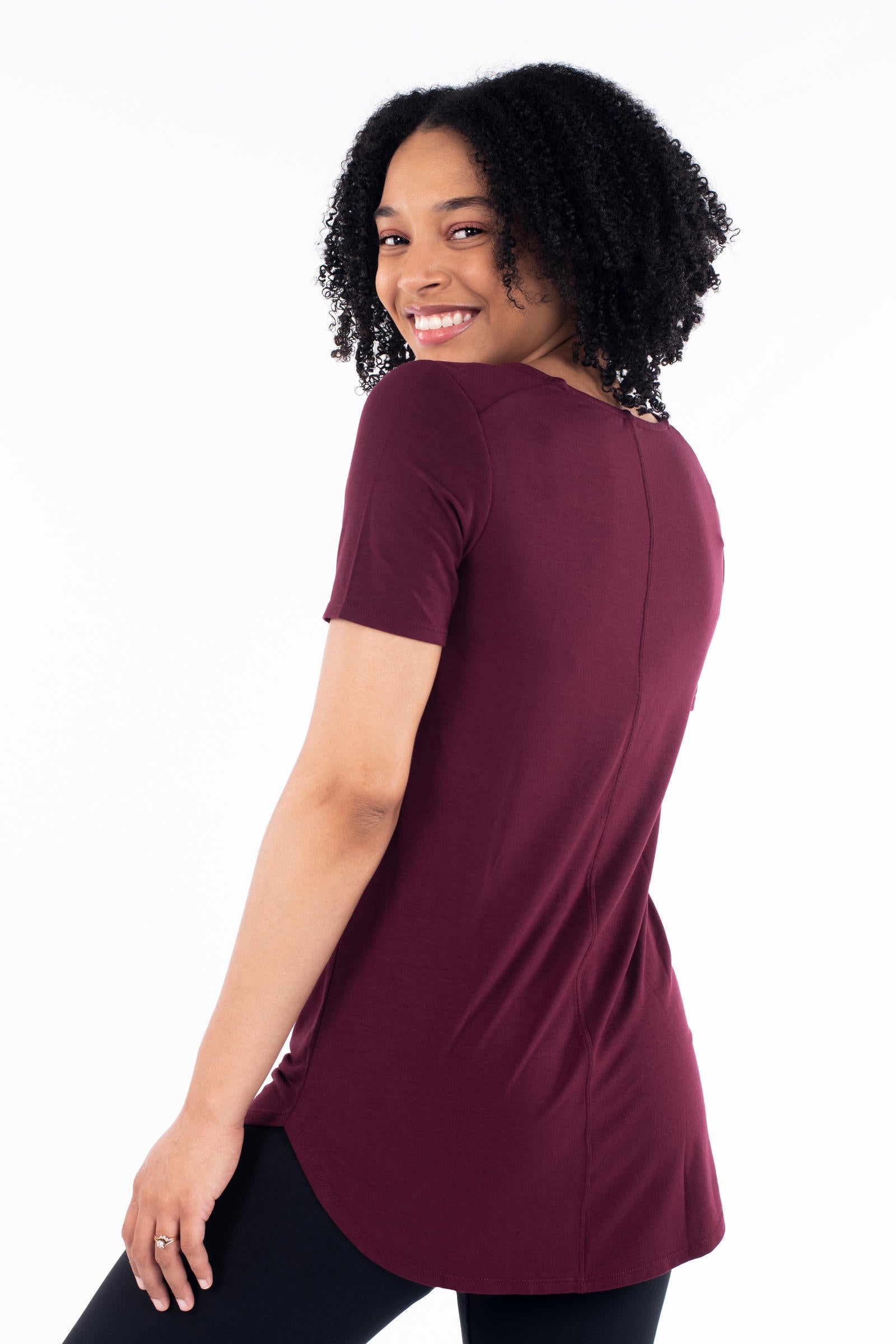 Woman smiling wearing maroon Classic Tee by SweetLegs Canada with short sleeves and rounded high-low hem back view