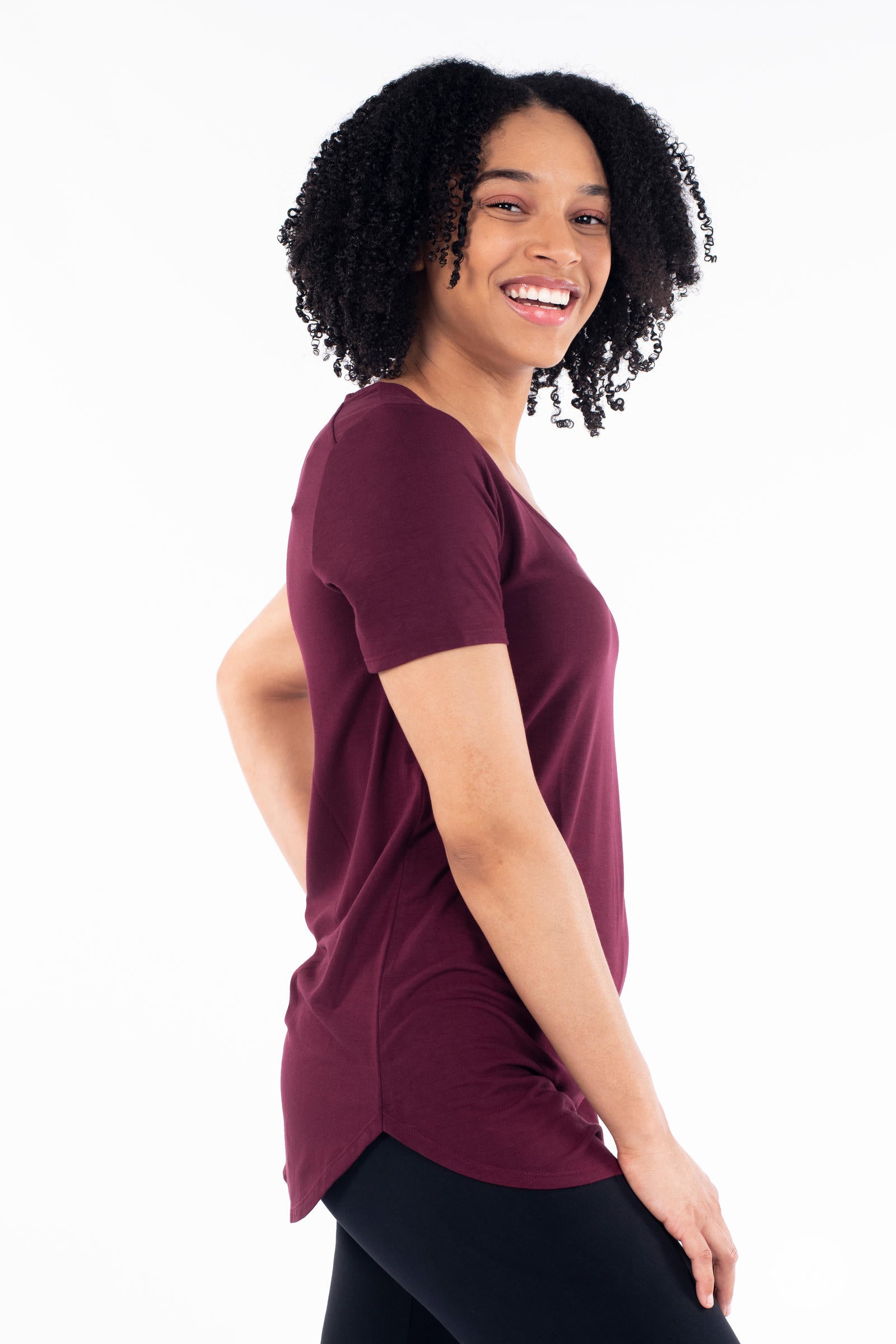 Smiling woman wearing maroon Classic Tee by SweetLegs Canada with short sleeves and high-low hem side profile view