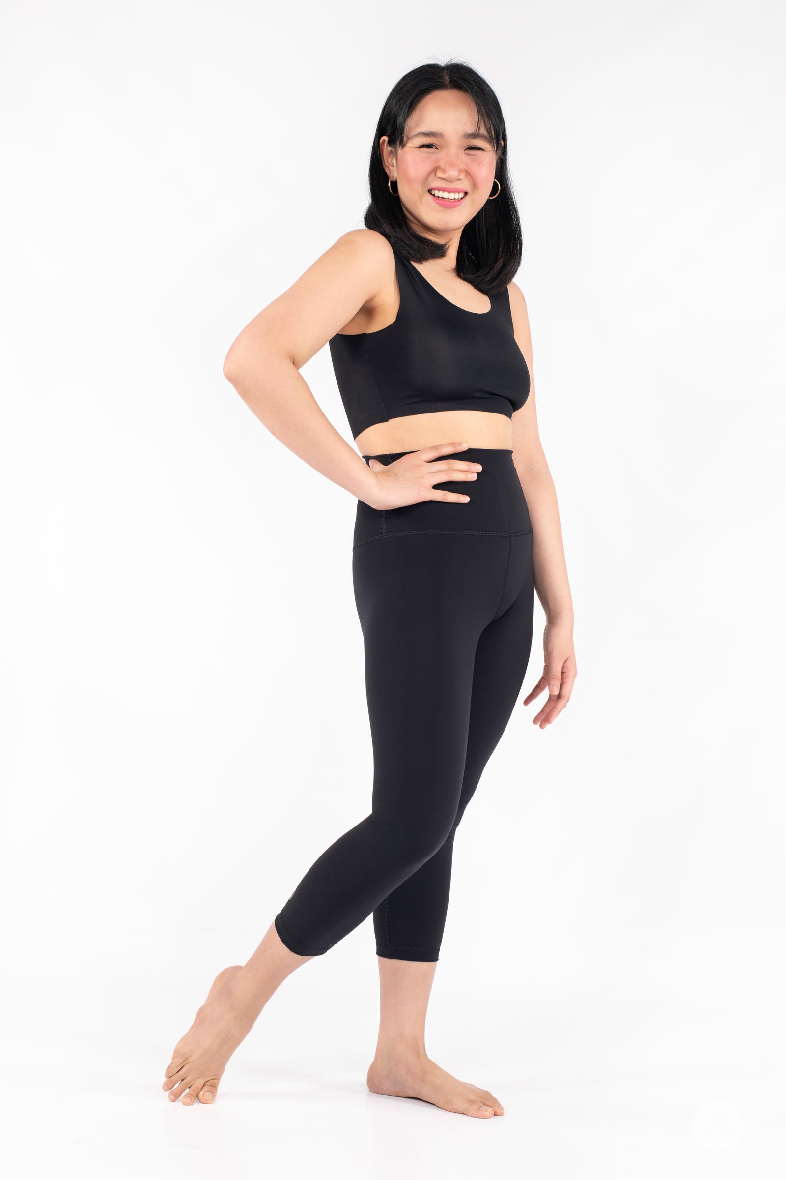 Smiling woman posing barefoot in side view wearing black Free Motion Crops by Athleisure SweetLegs collection