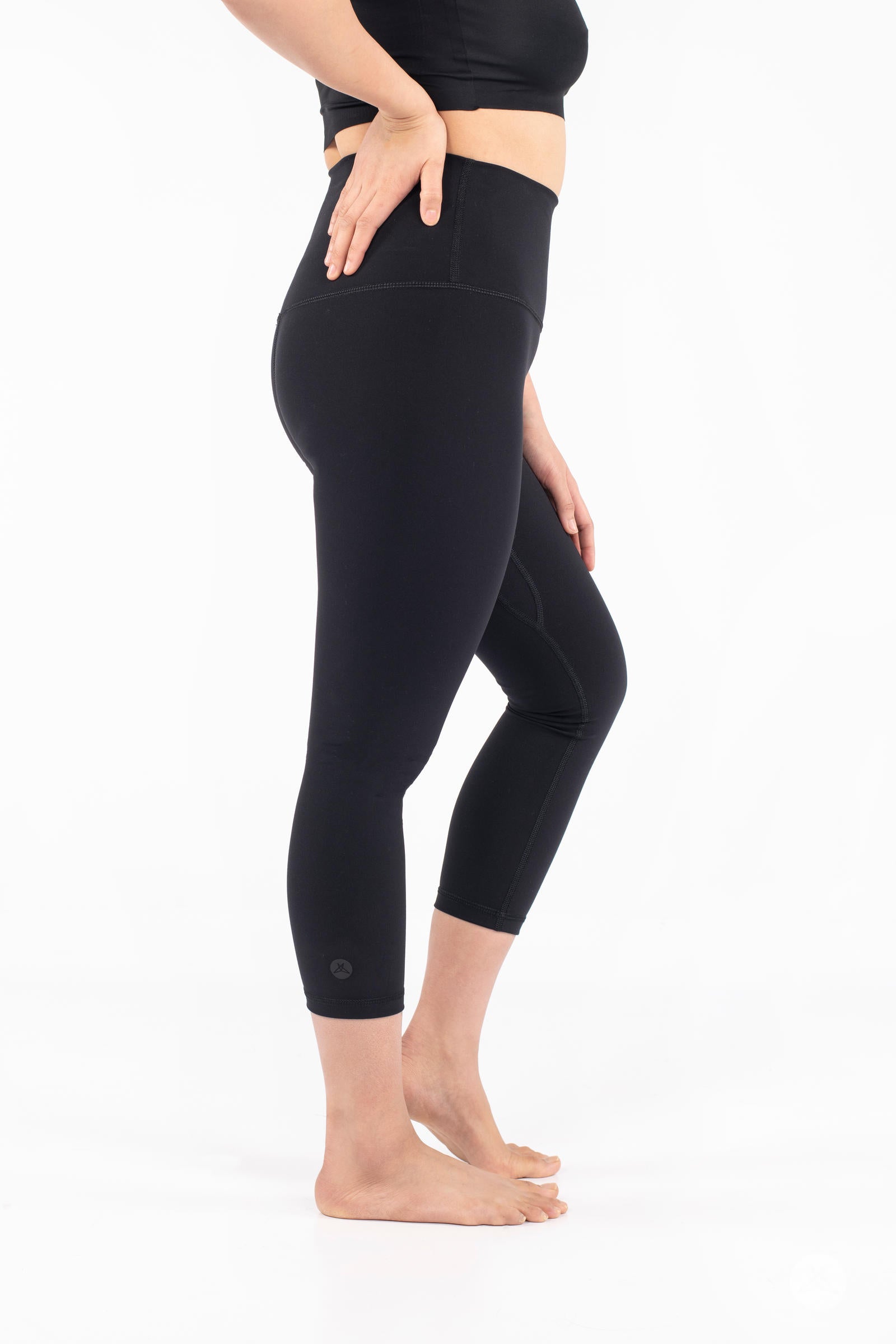 Side view of woman wearing black Free Motion Crops by Athleisure SweetLegs standing barefoot on white background