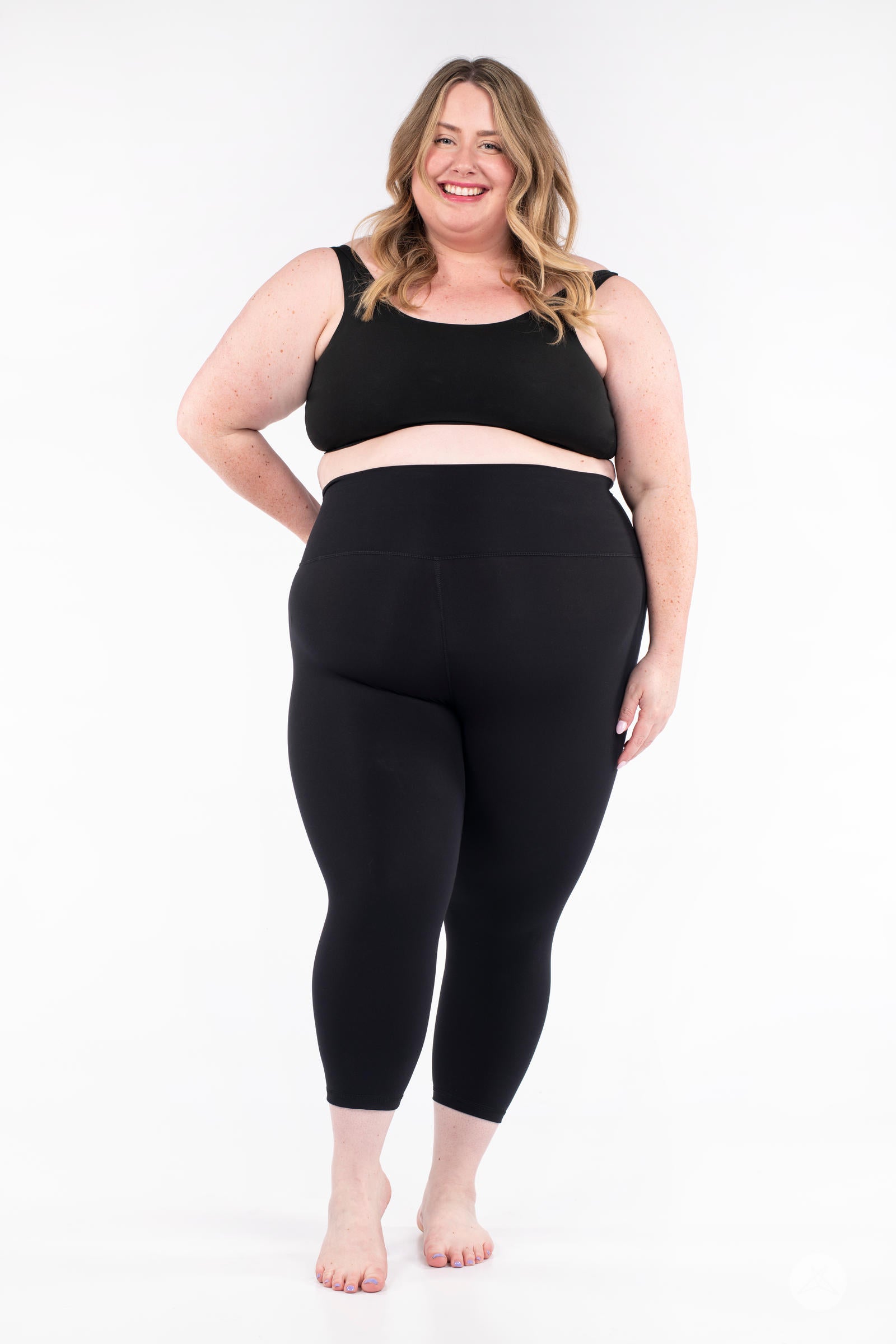 Plus-size model smiling wearing black Free Motion Crops by Athleisure SweetLegs standing barefoot front view