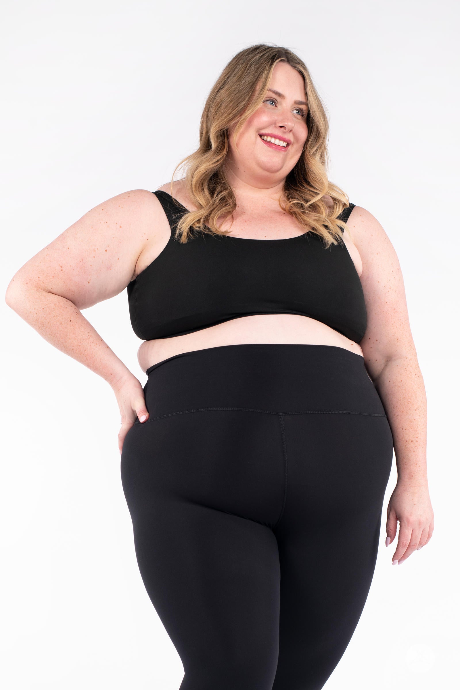 Plus-size model smiling wearing black Free Motion Crops by Athleisure SweetLegs in front view with hand on hip