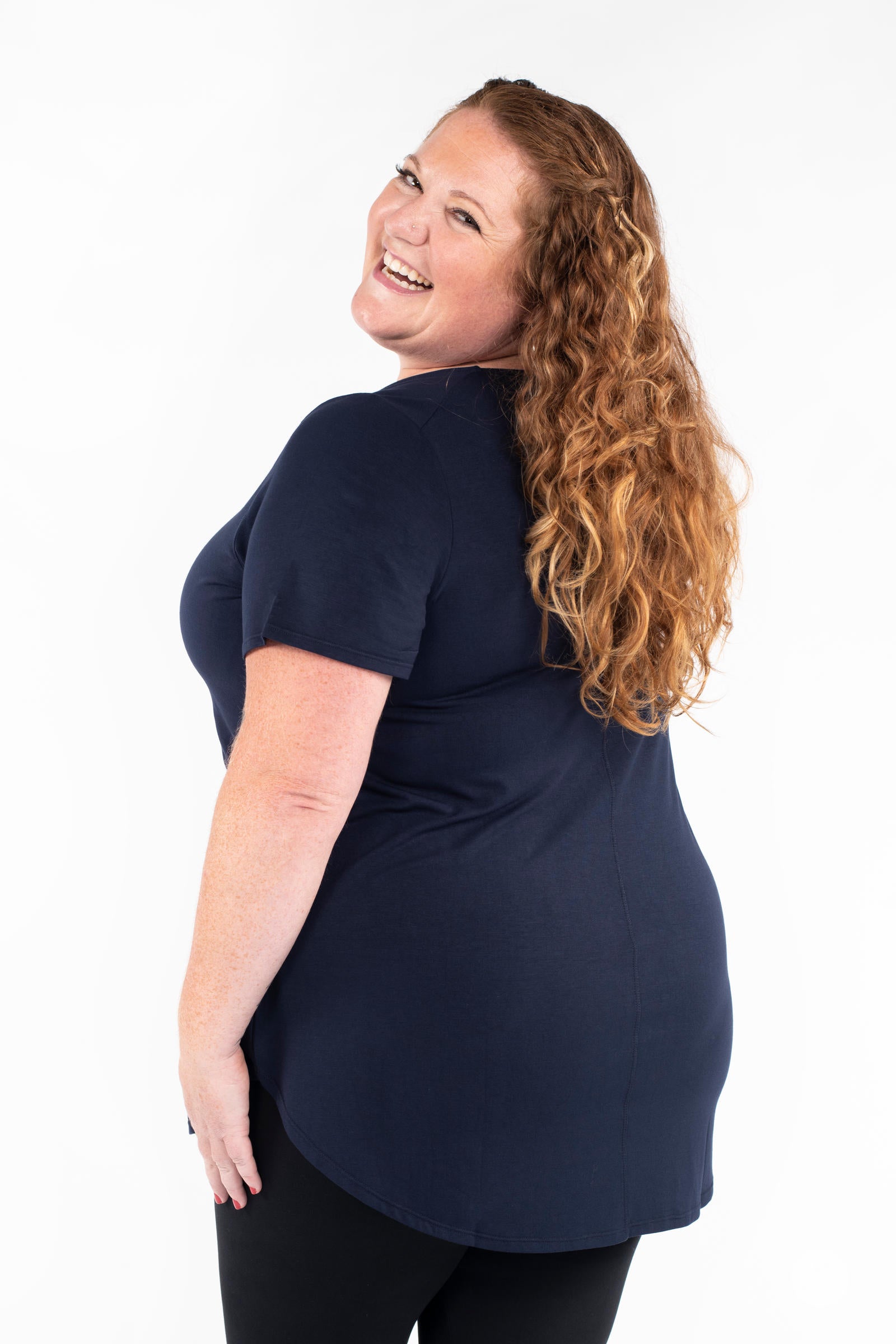 Plus size woman laughing wearing navy Classic Tee by SweetLegs Canada with short sleeves and curved hem back side view