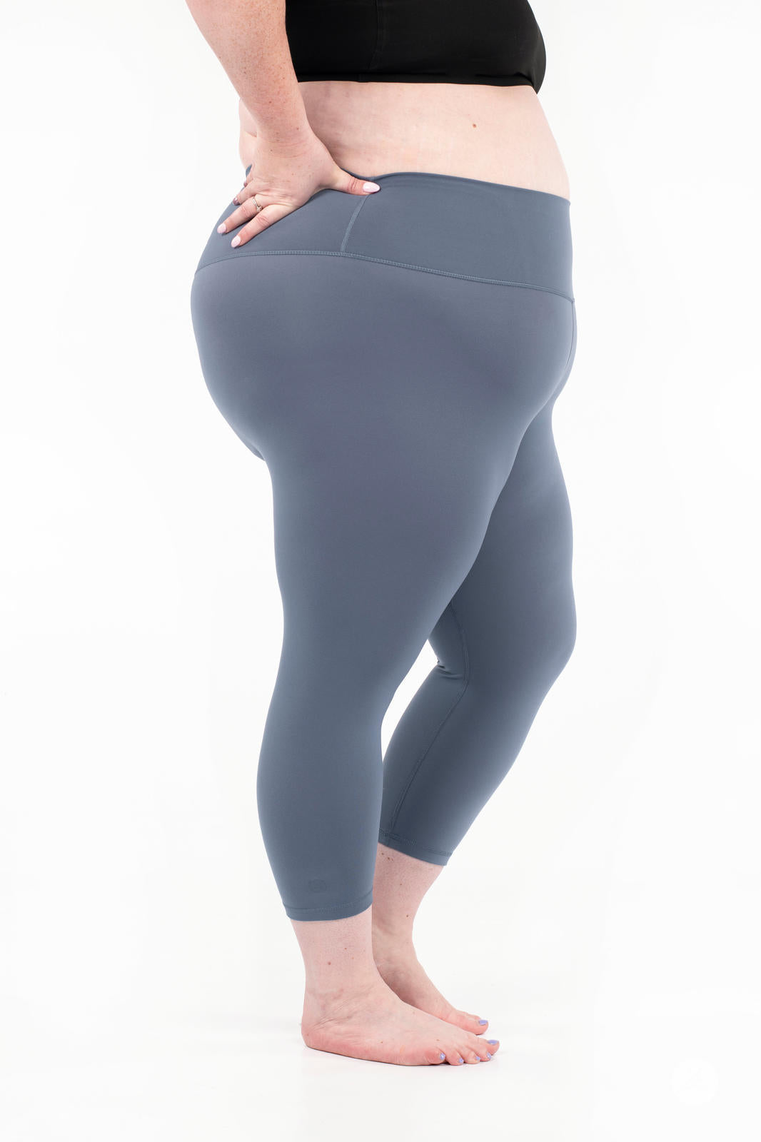 Side view of plus-size woman wearing gray Free Motion Crops by Athleisure SweetLegs standing barefoot on white background