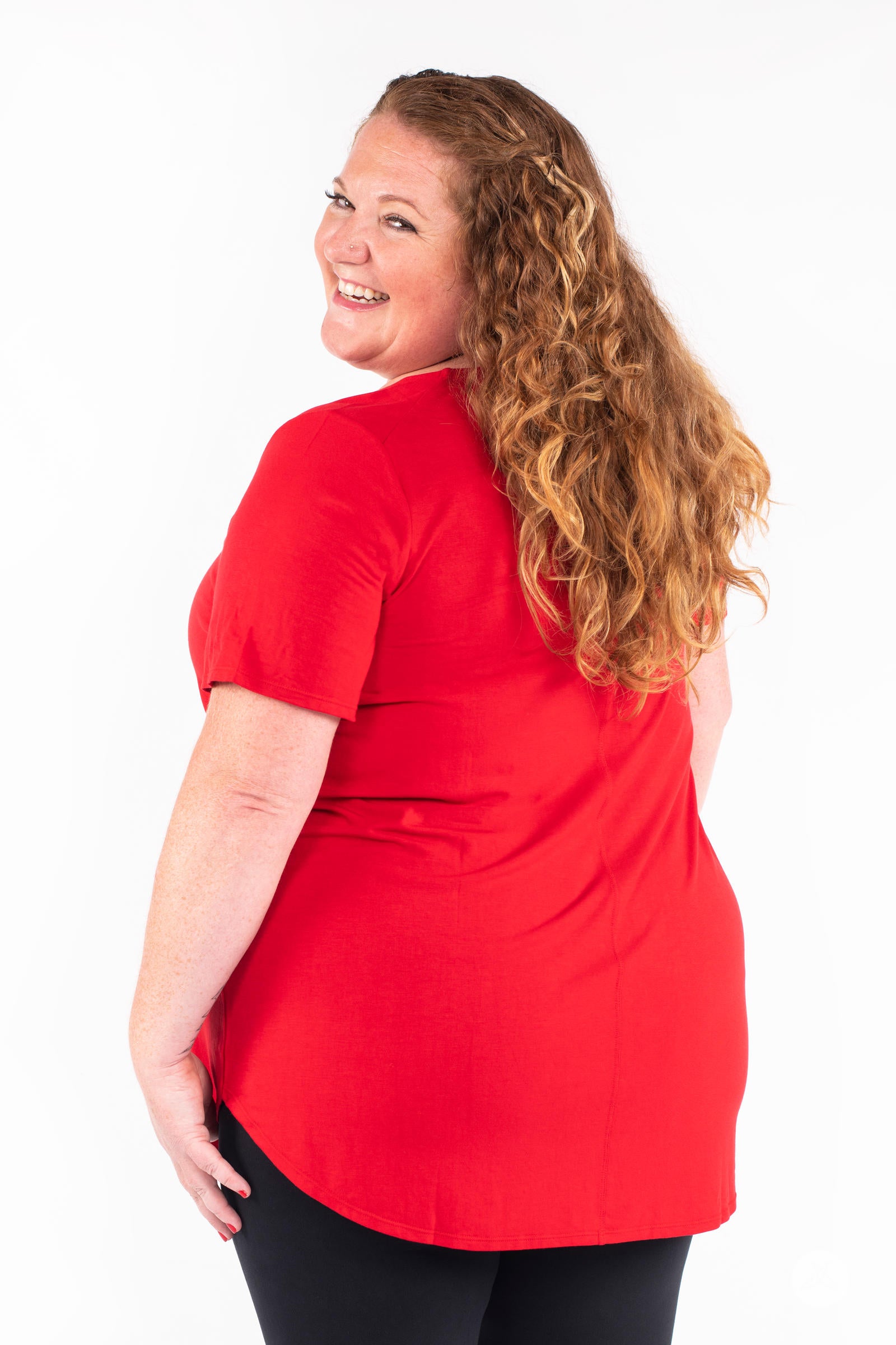 Plus size woman smiling wearing red Classic Tee by SweetLegs Canada with short sleeves and high to low hem back view