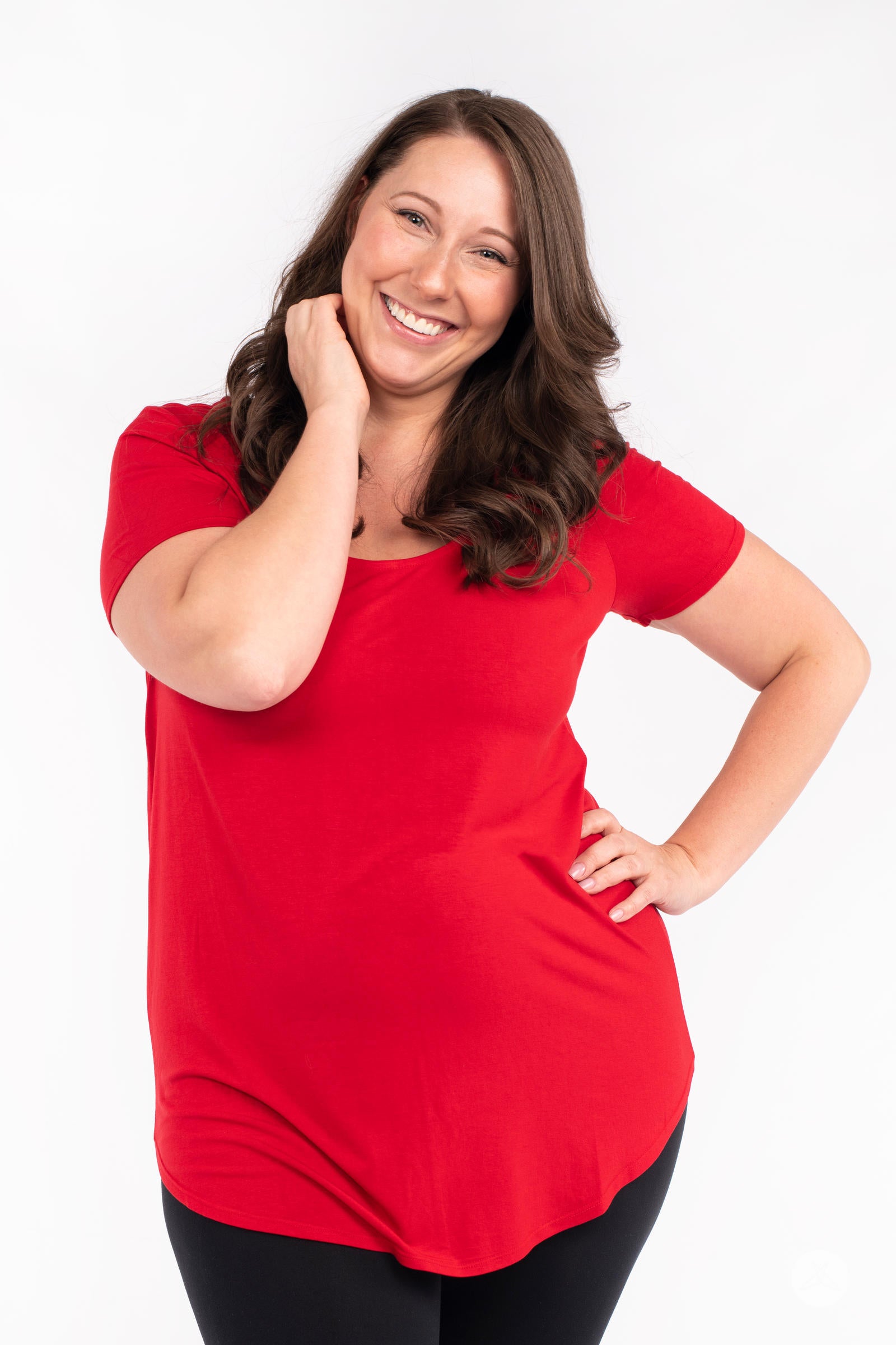 Smiling woman wearing red Classic Tee by SweetLegs Canada with scoop neck and relaxed fit, posing with hand near face