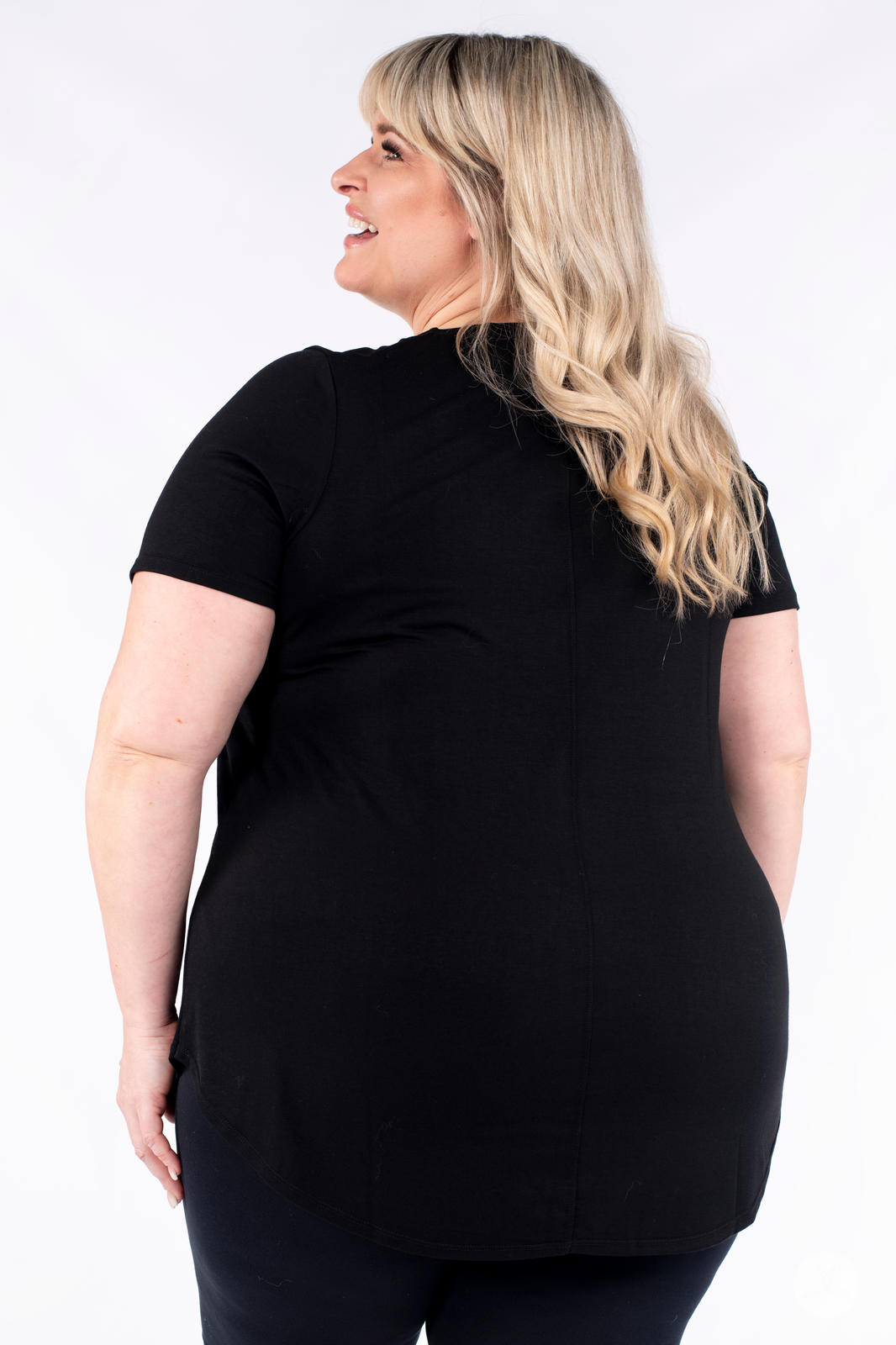 Plus size woman smiling wearing black Classic Tee by SweetLegs Canada with short sleeves and high-low hem back view