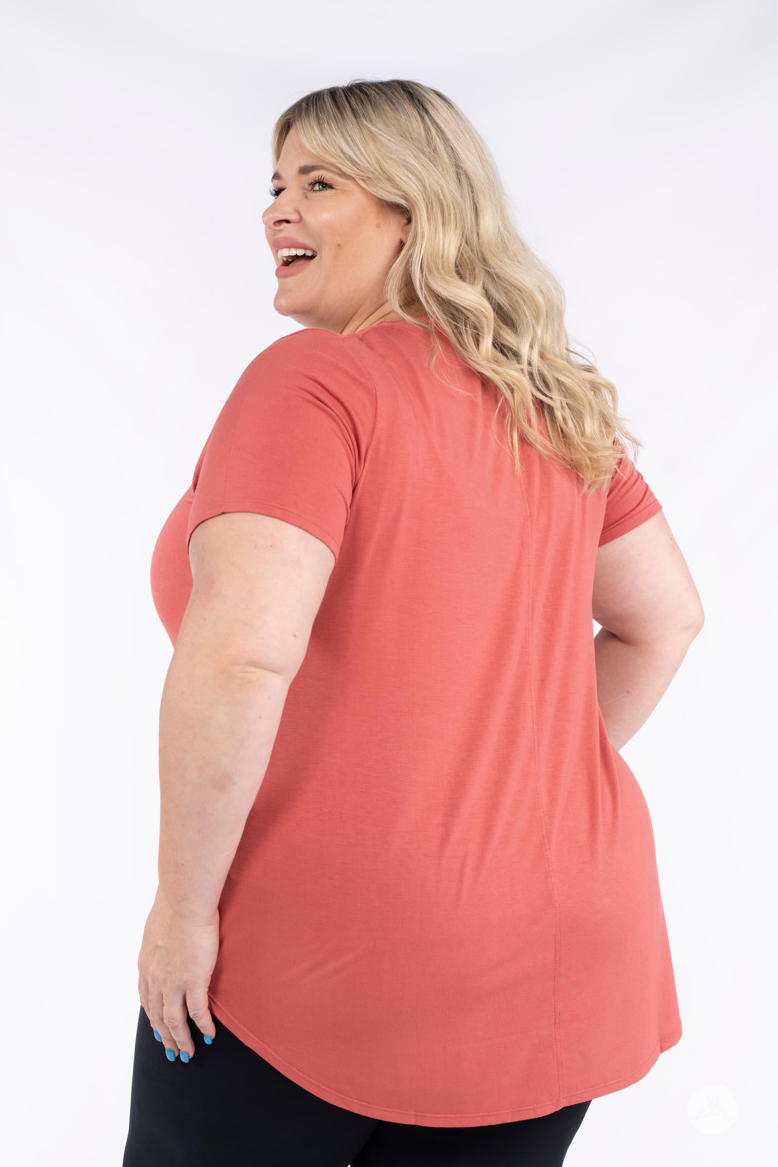 Plus size woman smiling wearing coral Classic Tee by SweetLegs Canada with short sleeves and high to low hem back view