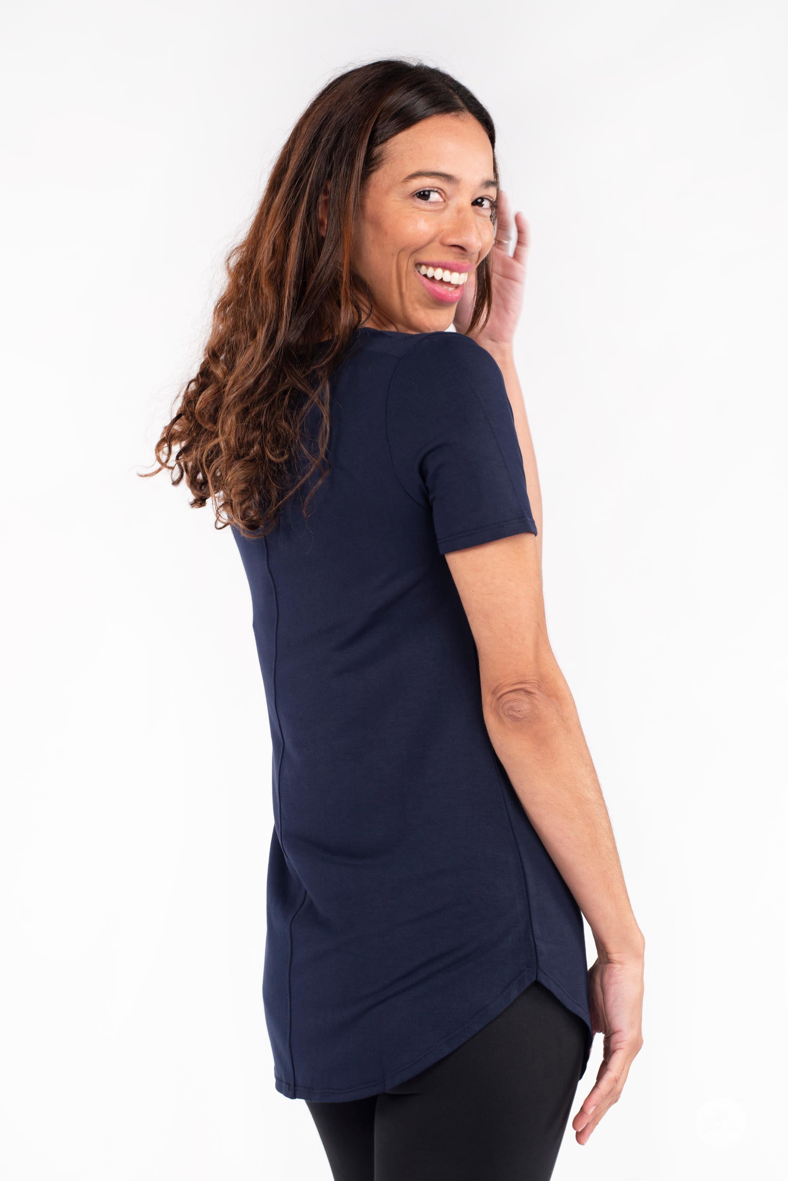 Woman smiling wearing navy Classic Tee by SweetLegs Canada with short sleeves and curved hem in back side view