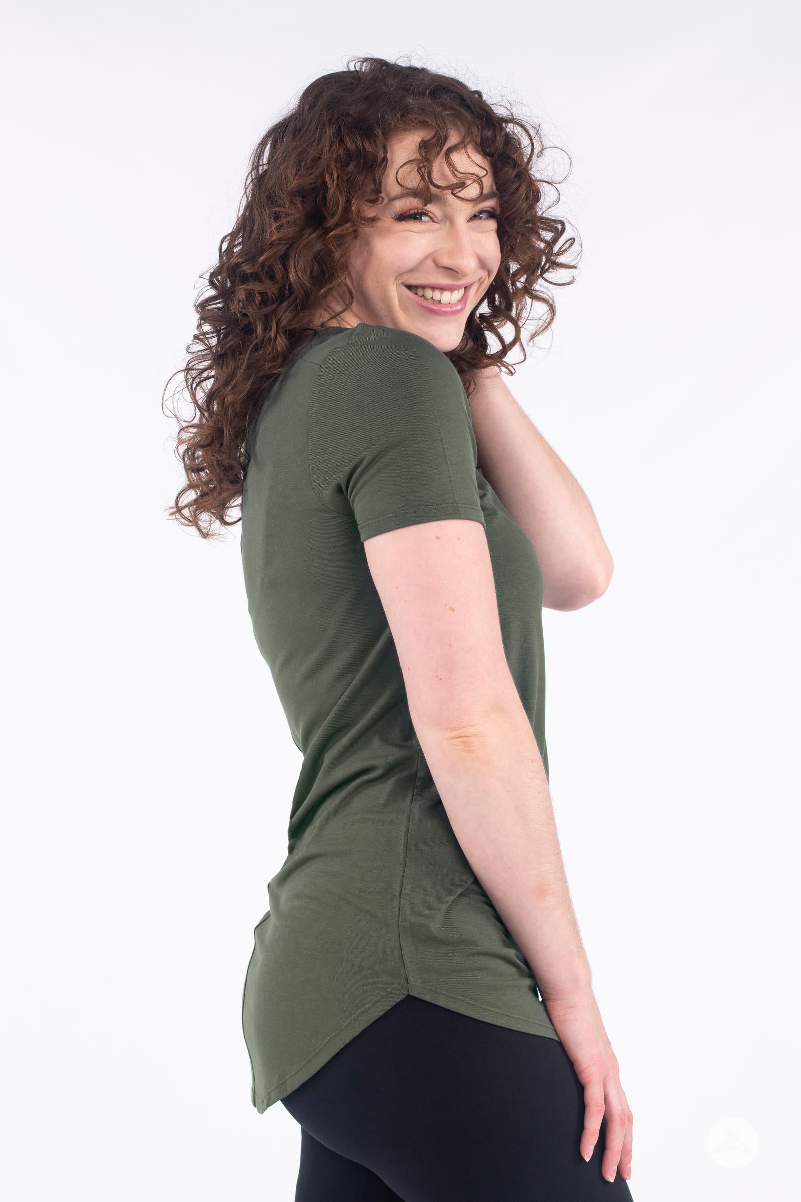 Smiling model in side pose wearing olive Classic Tee by SweetLegs Canada with high to low hem detail and short sleeves