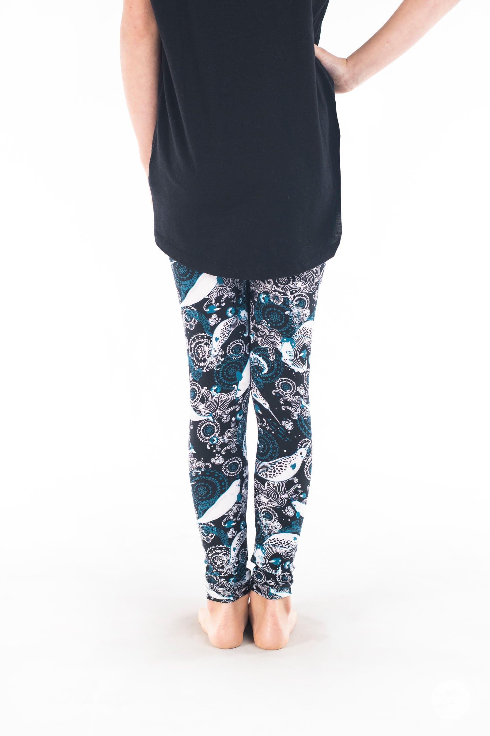 Child wearing SweetLegs Deep Blue Kids leggings with white beluga and teal ocean patterns on black background