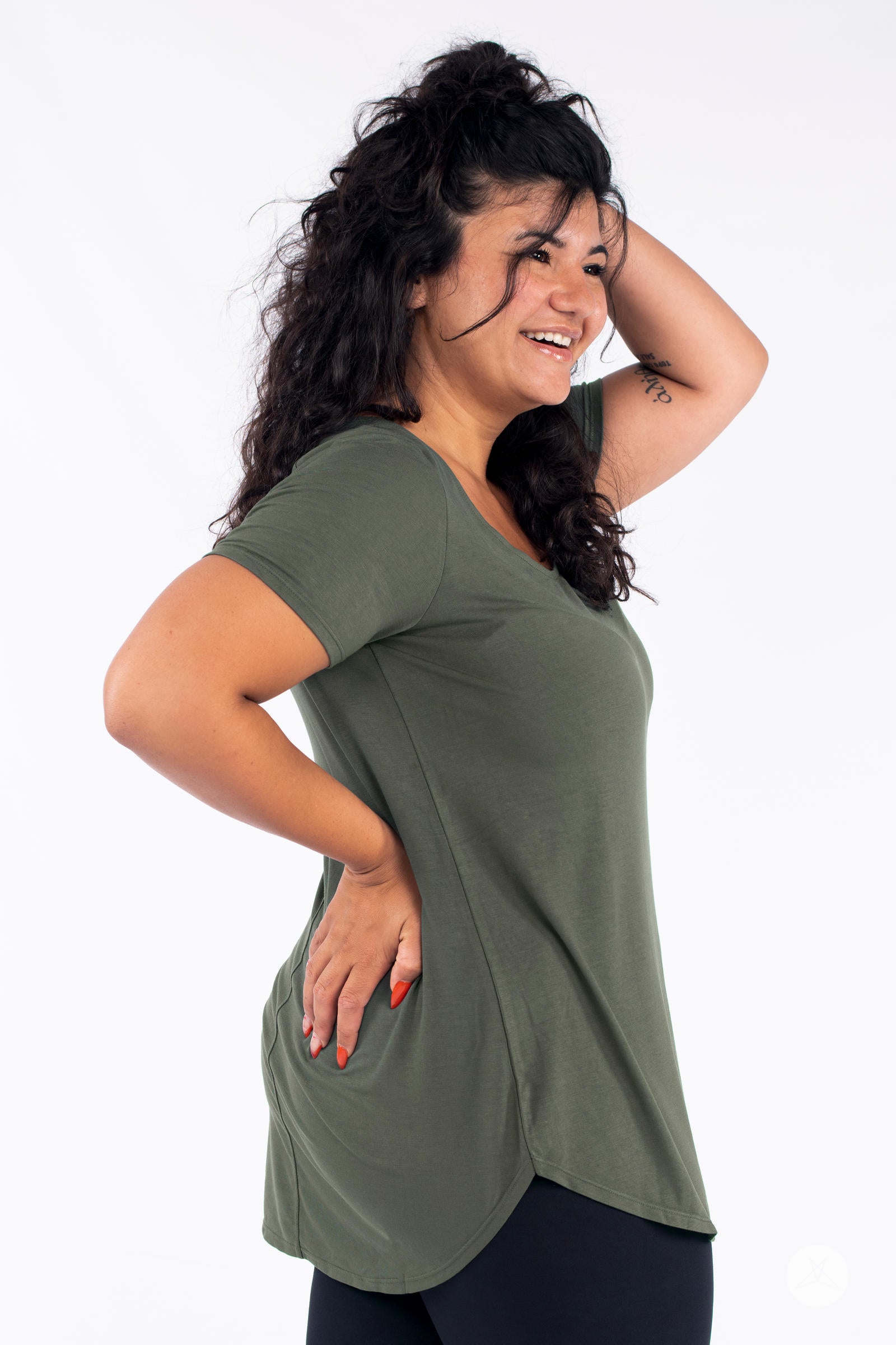 Smiling model wearing olive Classic Tee by SweetLegs Canada with scoop neckline and side seam details in profile view