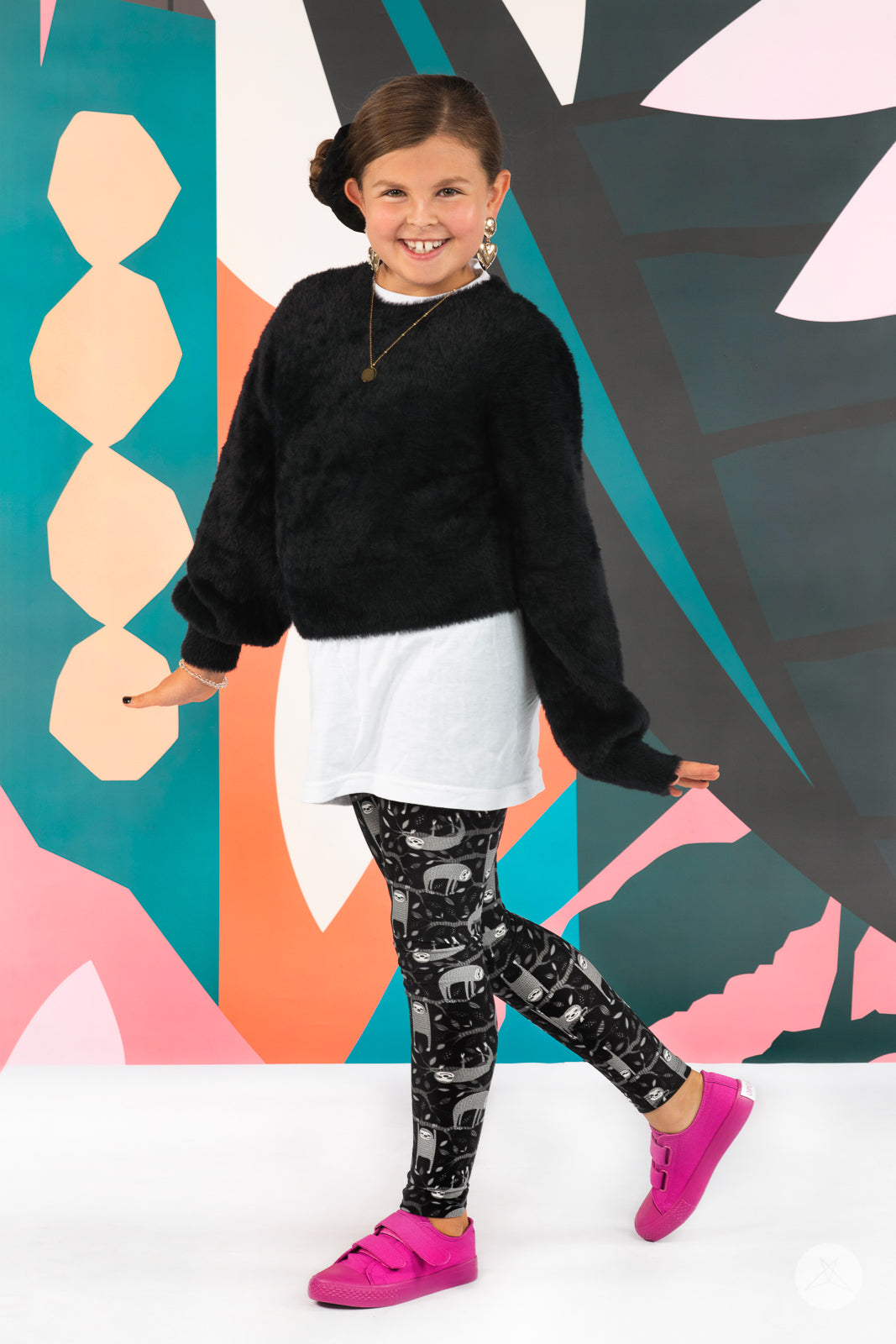 Smiling child wearing SweetLegs Hang In There Kids leggings with grey sloth print posing against colorful background