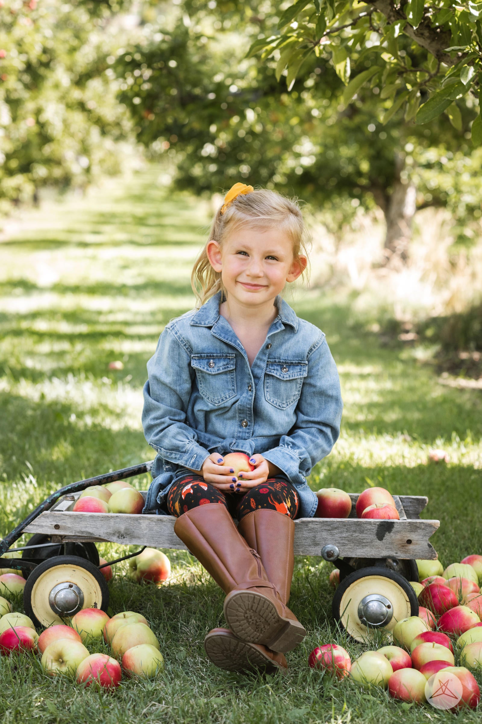 Young girl outdoors sitting on a wooden wagon surrounded by apples wearing SweetLegs Pumpkin Spice Kids leggings with autumnal fox print