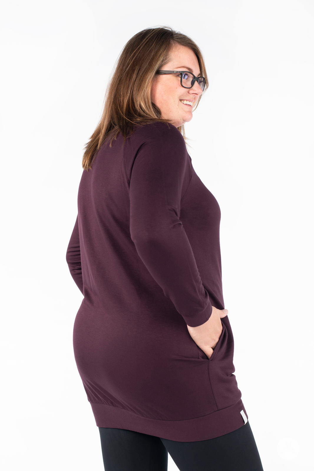 Side angle of SweetLegs Canada Everyday Raglan Pullover in dark plum worn by smiling model with hands in pockets