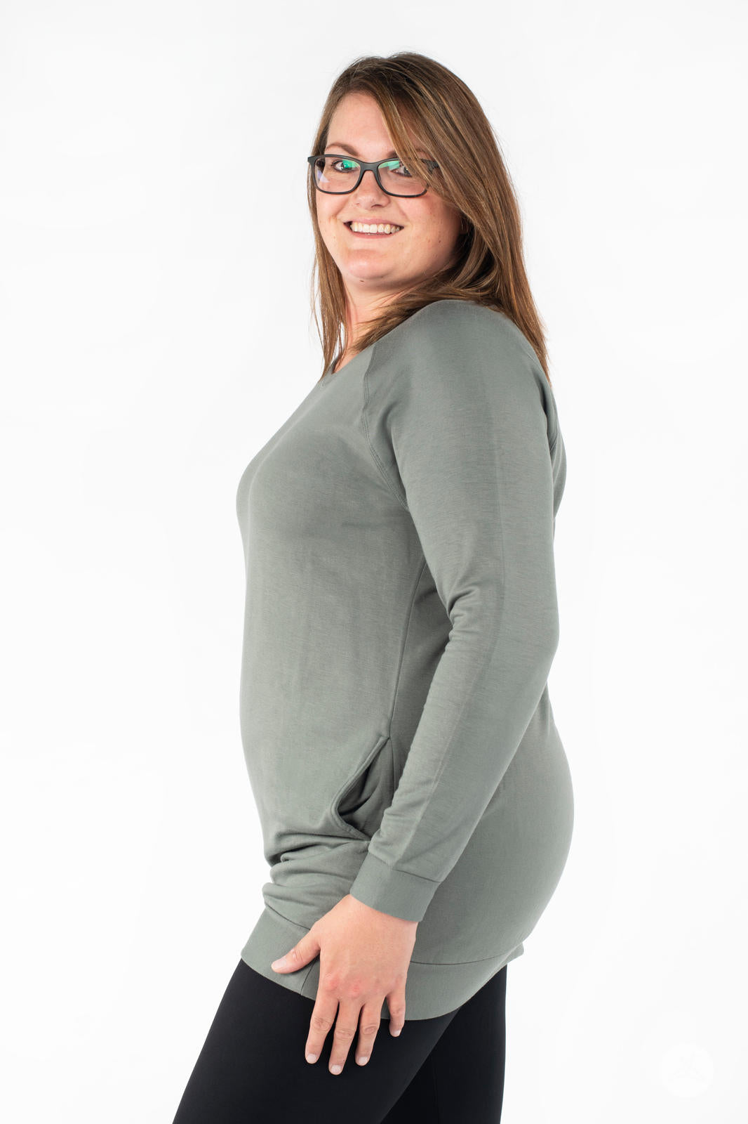 Smiling model wearing SweetLegs Canada Everyday Raglan Pullover in muted green with hand resting by thigh in profile view