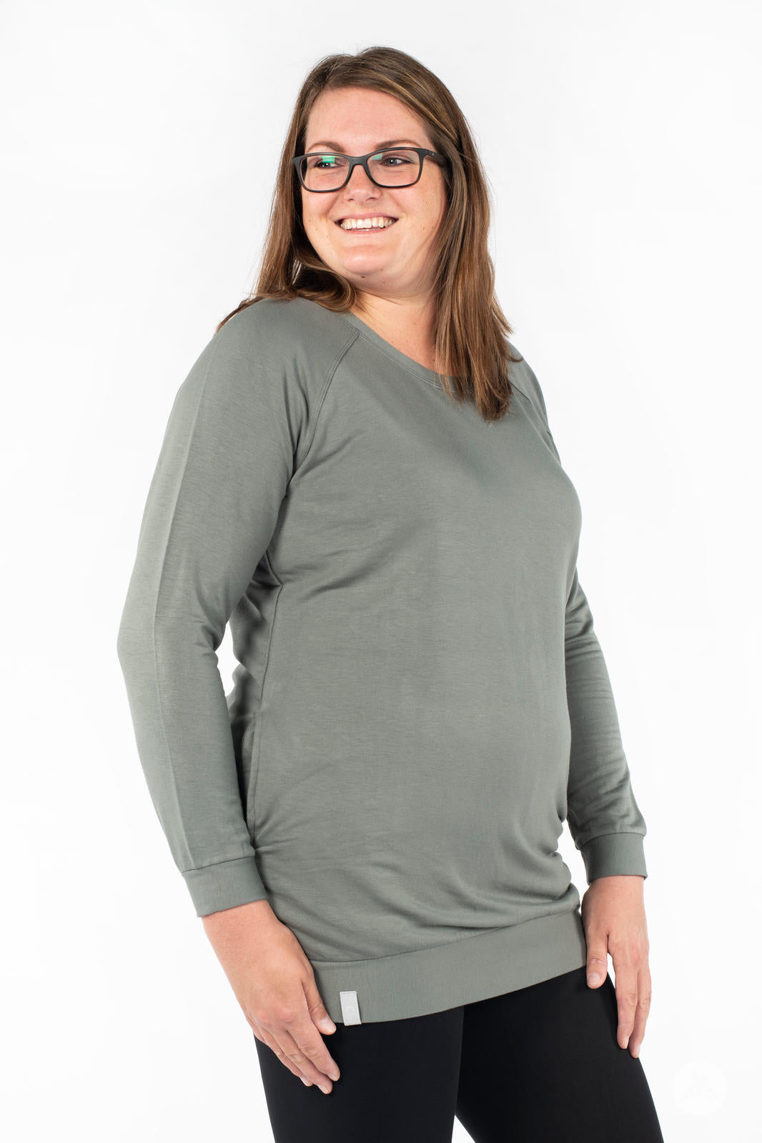 Plus-size woman smiling wearing SweetLegs Canada Everyday Raglan Pullover in muted green with relaxed side pose