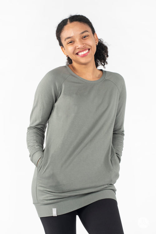 Model smiling wearing SweetLegs Canada Everyday Raglan Pullover in muted green with hands in pockets and relaxed posture