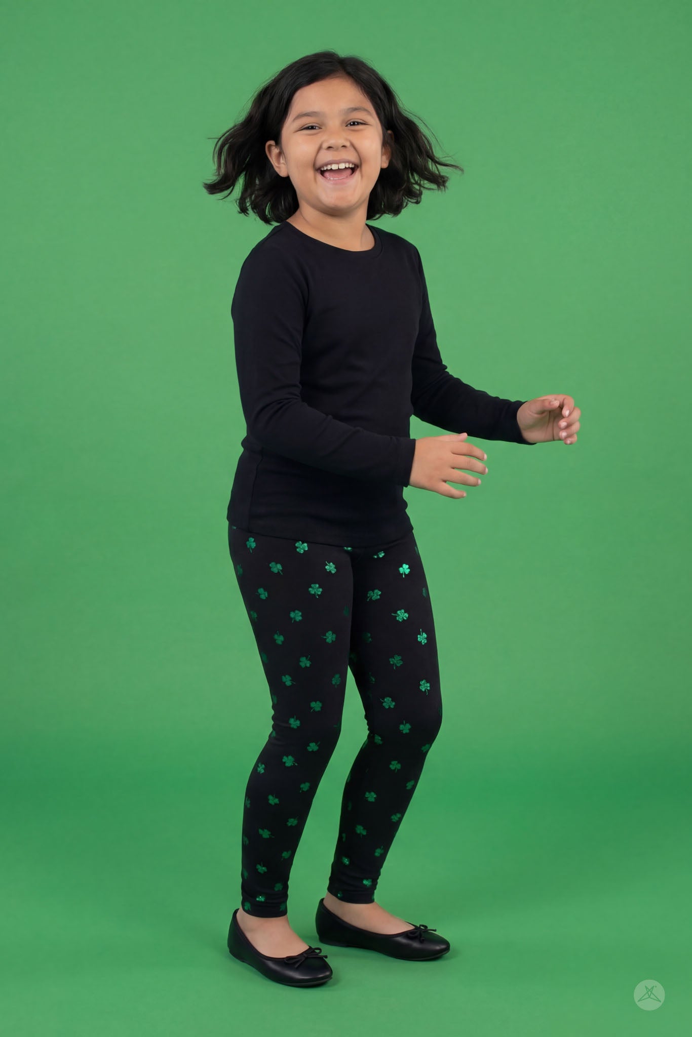 Happy child wearing Lucky Glow Kids leggings with emerald shamrock print by SweetLegs on green background