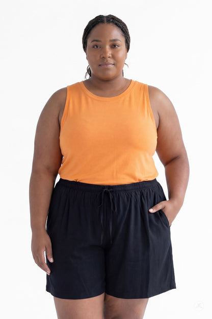 Plus size model wearing SweetLegs Breeze Shorts in black with elastic waistband and pockets paired with orange sleeveless top