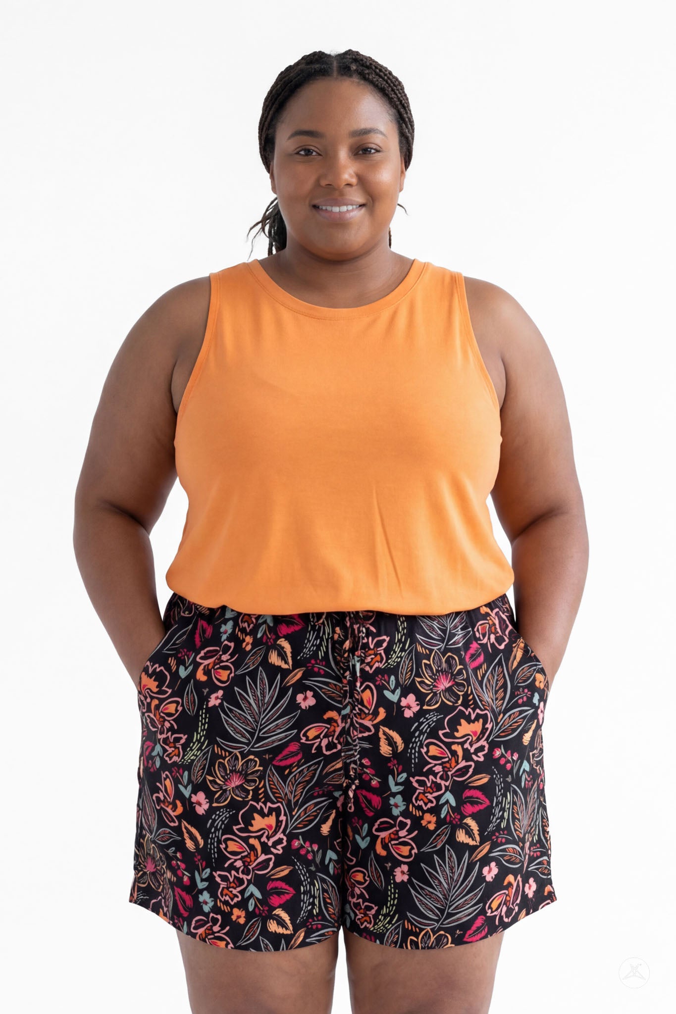 Plus size woman wearing SweetLegs Breeze Shorts with colorful floral print and orange sleeveless top, hands in pockets