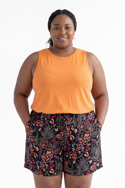 Plus size woman wearing SweetLegs Breeze Shorts with colorful floral print and orange sleeveless top, hands in pockets