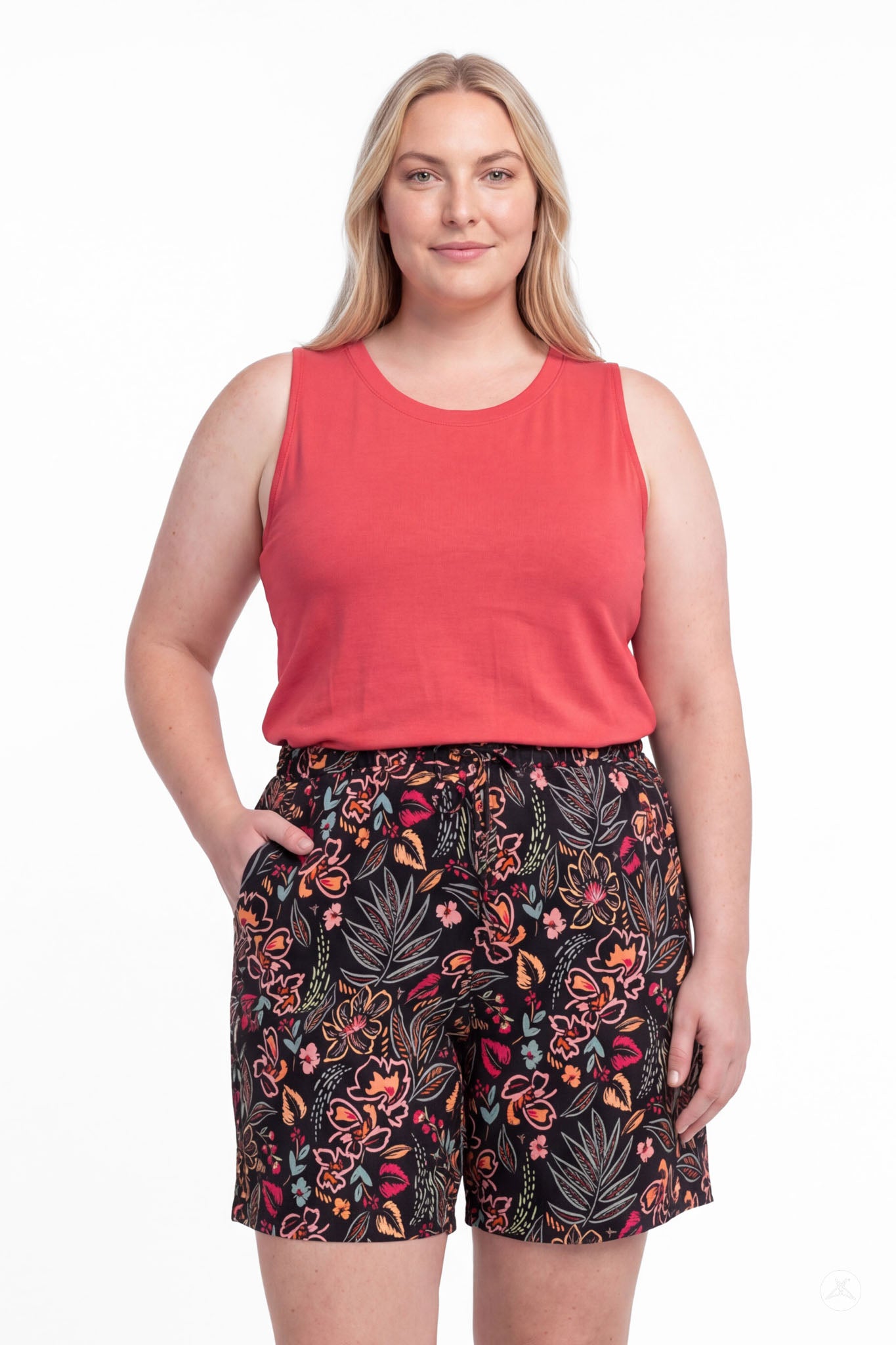 Plus size woman wearing SweetLegs Breeze Shorts with floral pattern and coral sleeveless top, hands in pockets, front view
