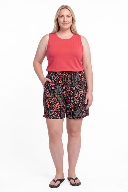 Plus size woman wearing SweetLegs Breeze Shorts with dark floral pattern and coral sleeveless top, front view with hands in pockets