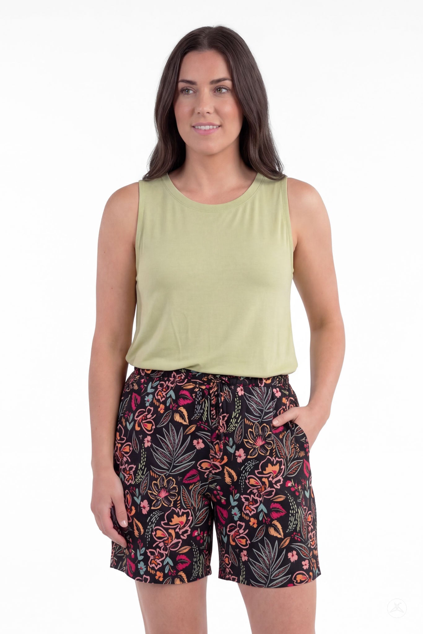 Woman wearing SweetLegs Breeze Shorts with black floral pattern and light green sleeveless top, hand in pocket, standing