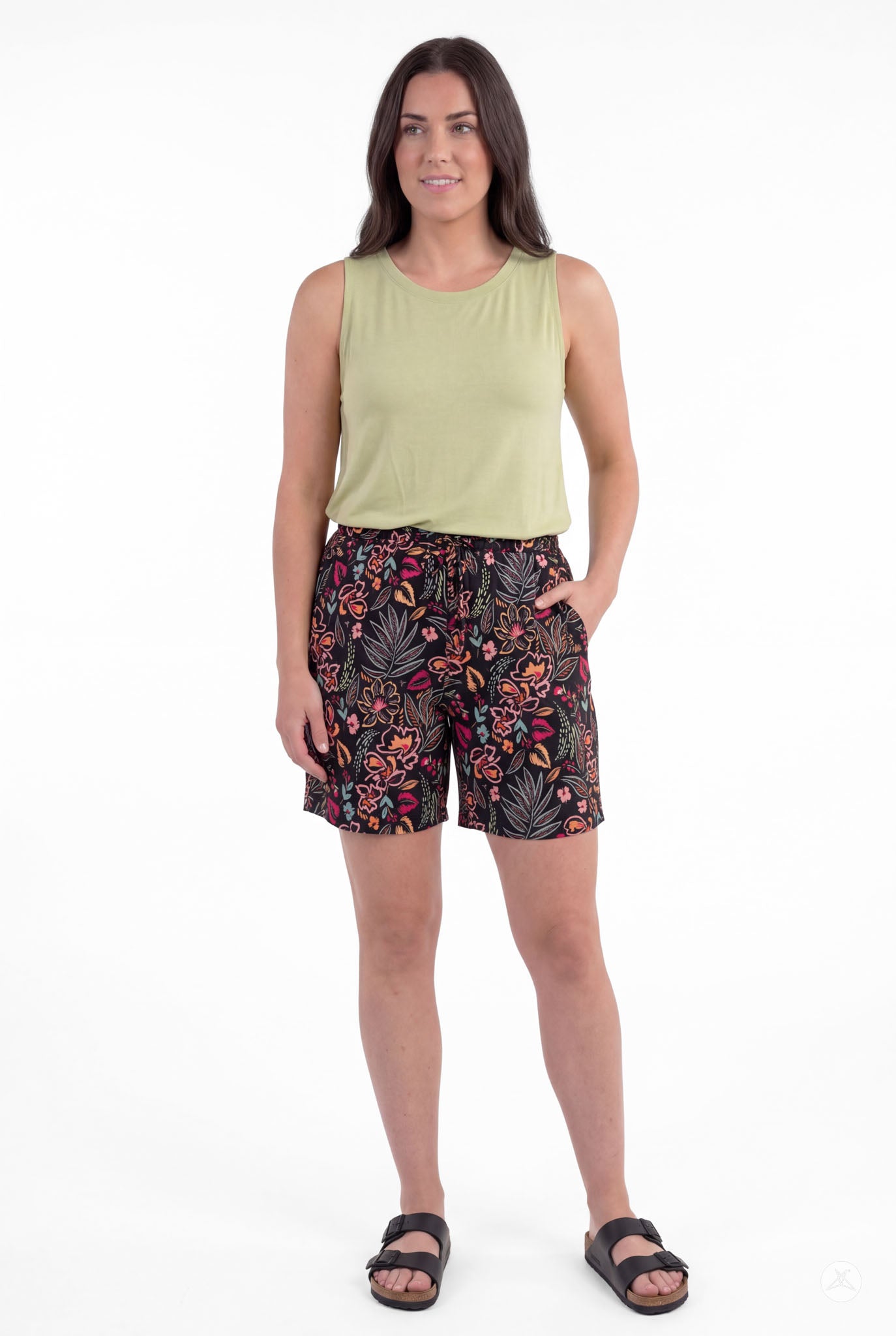 Woman wearing SweetLegs Breeze Shorts with colorful floral pattern and light green sleeveless top, hands in pockets, standing