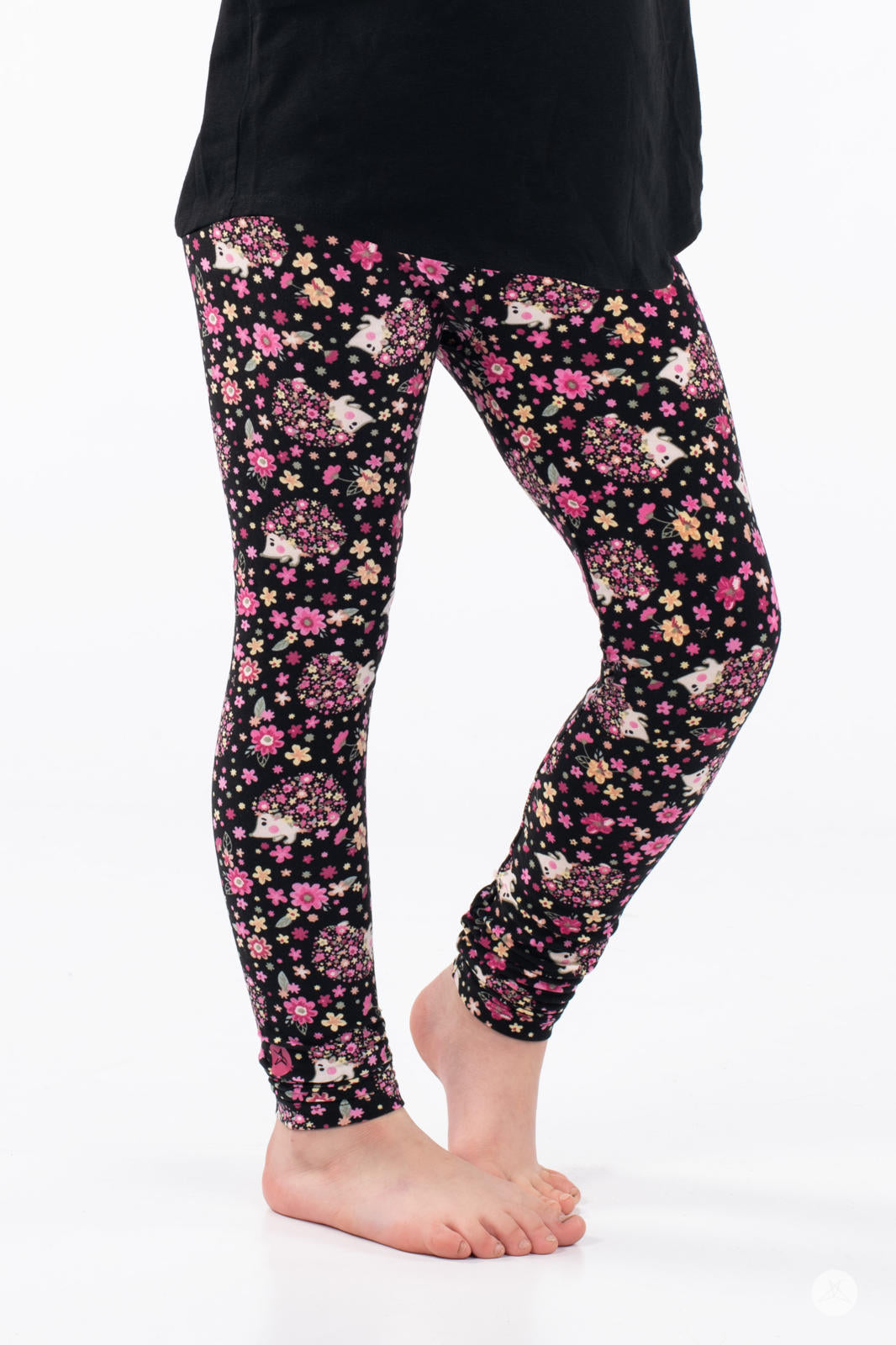 Child wearing SweetLegs Vault - Kids leggings with pink floral and hedgehog pattern on black background barefoot