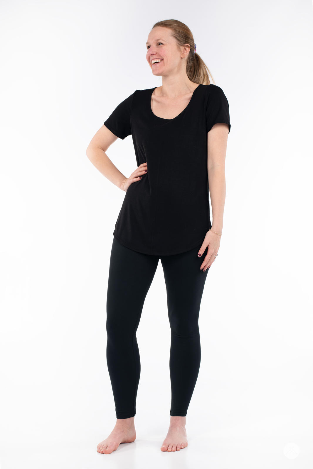 Woman standing barefoot wearing SweetLegs Black Licorice leggings and black short sleeve top smiling on white background
