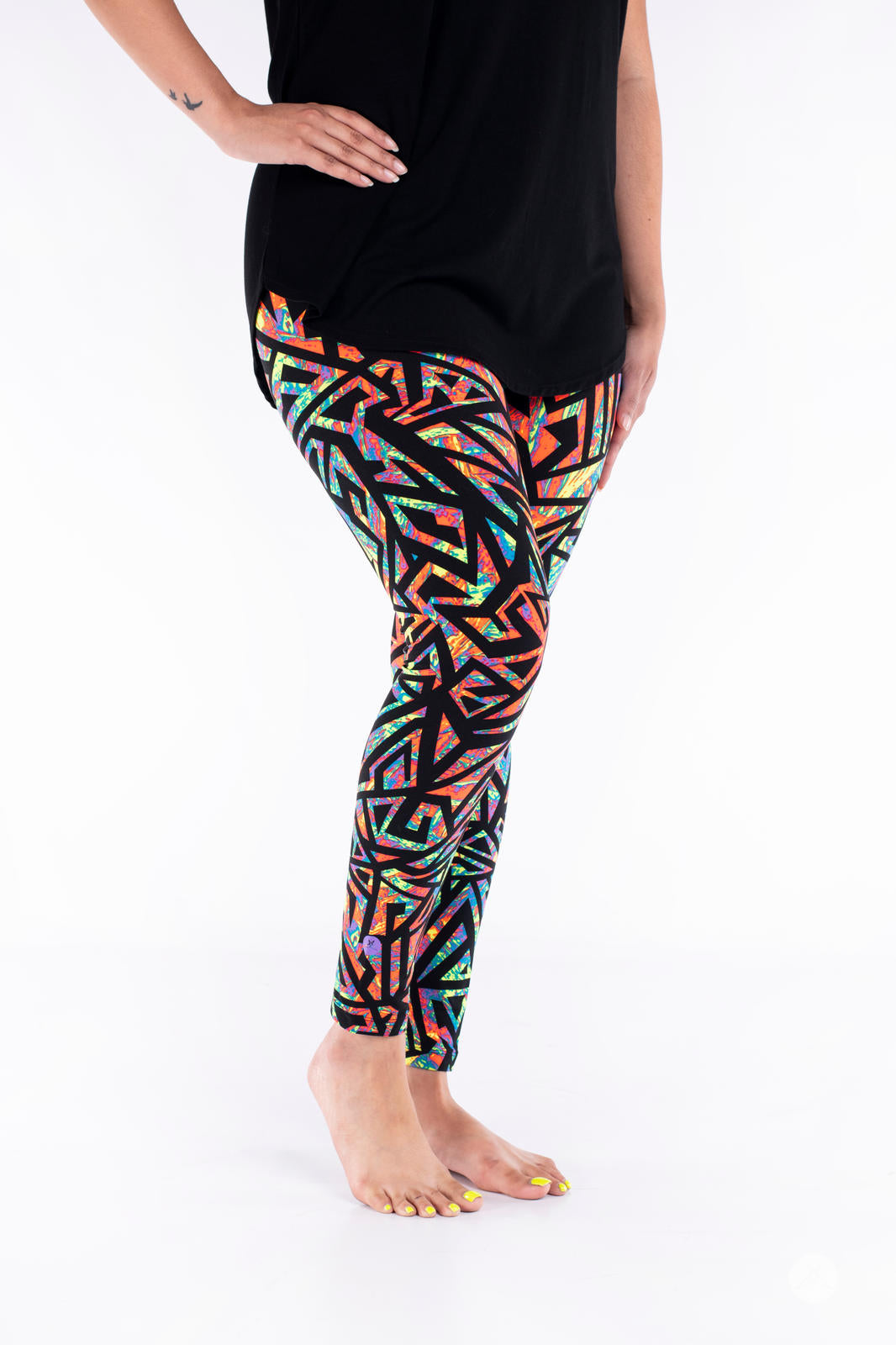Plus size model wearing Vault - Signature Leggings by SweetLegs with vibrant multicolor geometric pattern barefoot