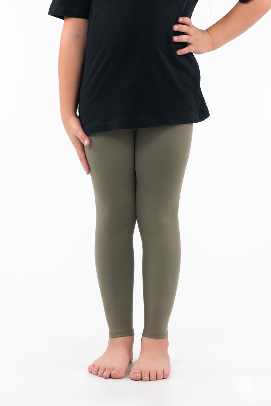 Child wearing SweetLegs Olive Kids leggings paired with black top standing barefoot on white background