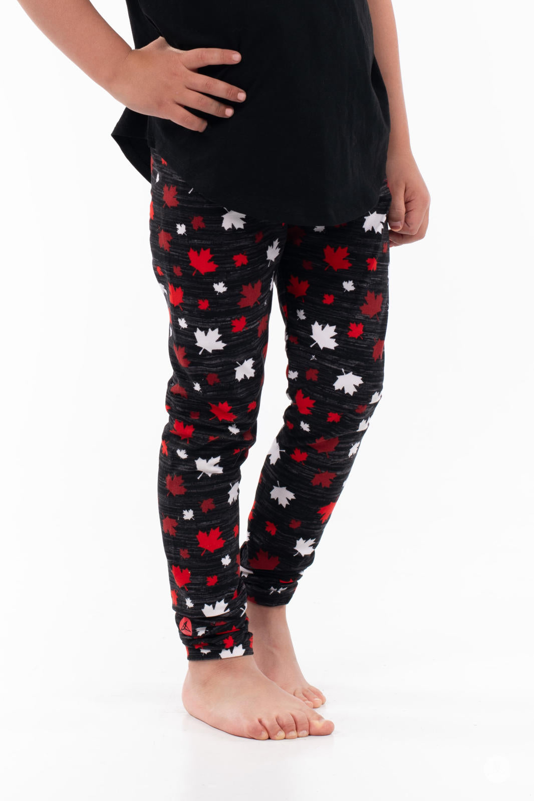 Child wearing Vault - Kids leggings by SweetLegs with red and white maple leaf pattern on black barefoot