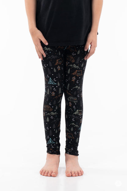 Child wearing Vault - Kids leggings by SweetLegs with camping, mountains, and trees pattern on black barefoot