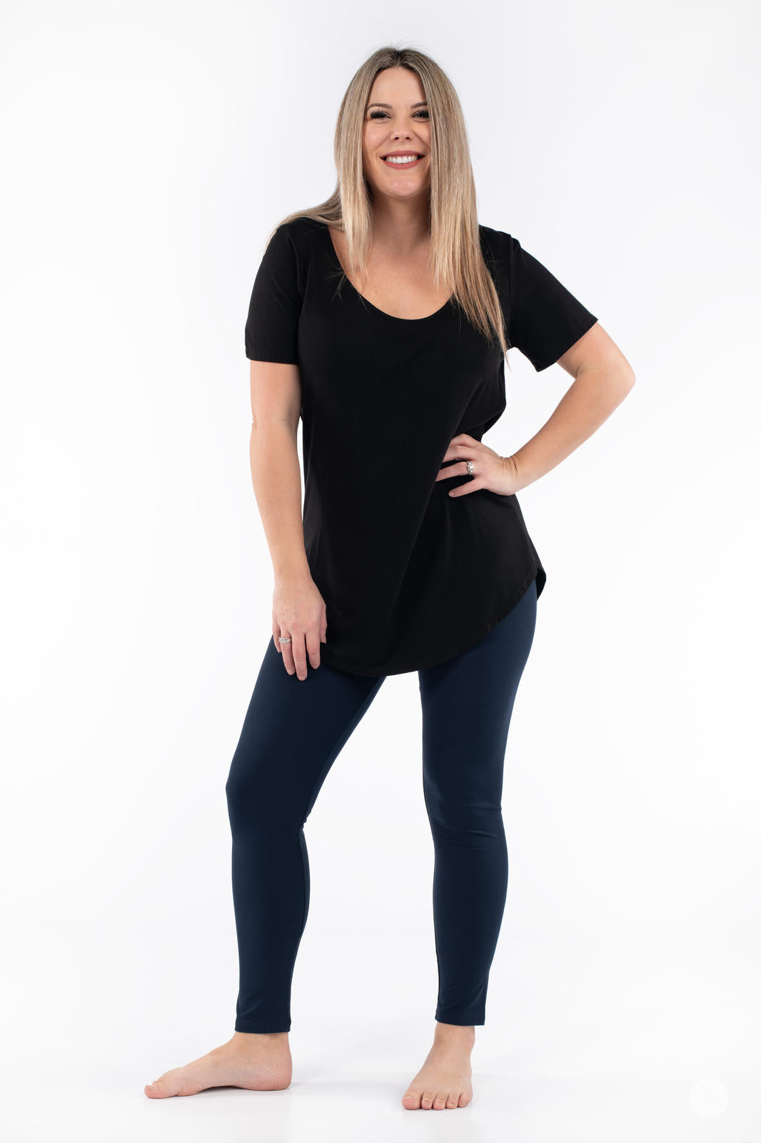 Smiling woman standing barefoot wearing Navy leggings by SweetLegs paired with black short-sleeve top on white background