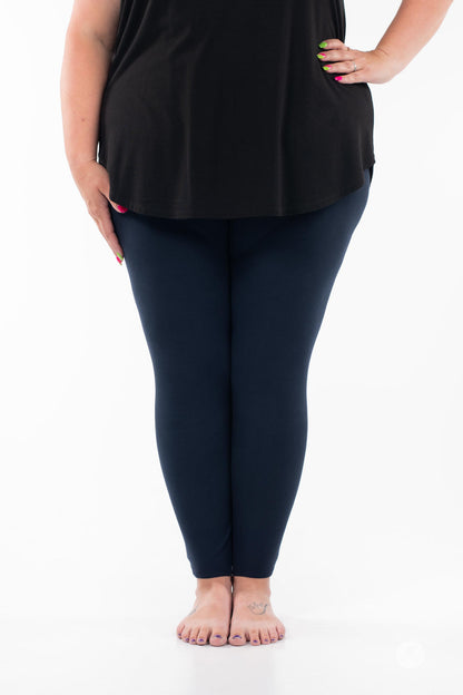 Plus-size model wearing Navy leggings by SweetLegs paired with black top standing barefoot on white background