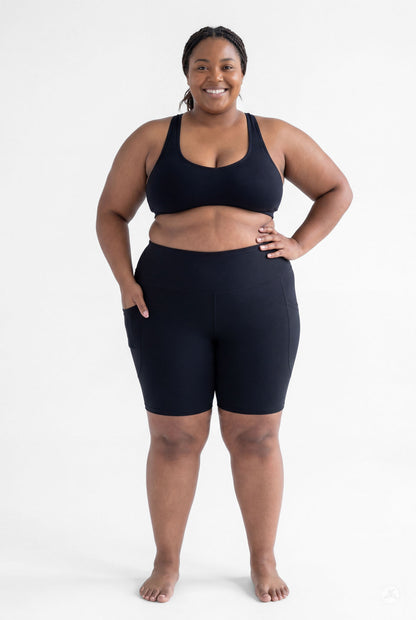 Plus size model smiling wearing SweetLegs Black High-Waisted Pocket Biker Shorts with hand in side pocket front view