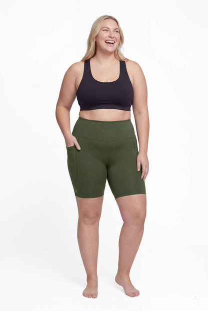 Plus size model wearing SweetLegs Cedar High-Waisted Pocket Biker Shorts in green with black sports bra front view