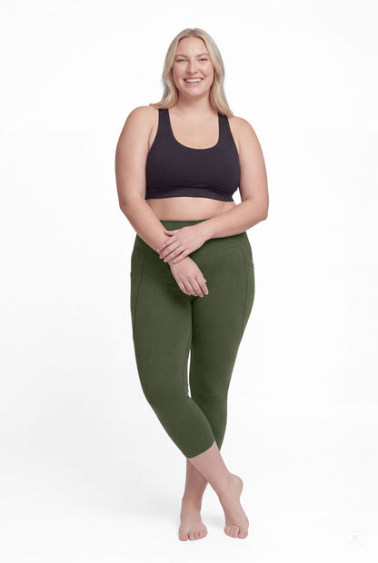 Smiling woman standing barefoot wearing SweetLegs Cedar High-Waisted Pocket Crops in green with black sports bra