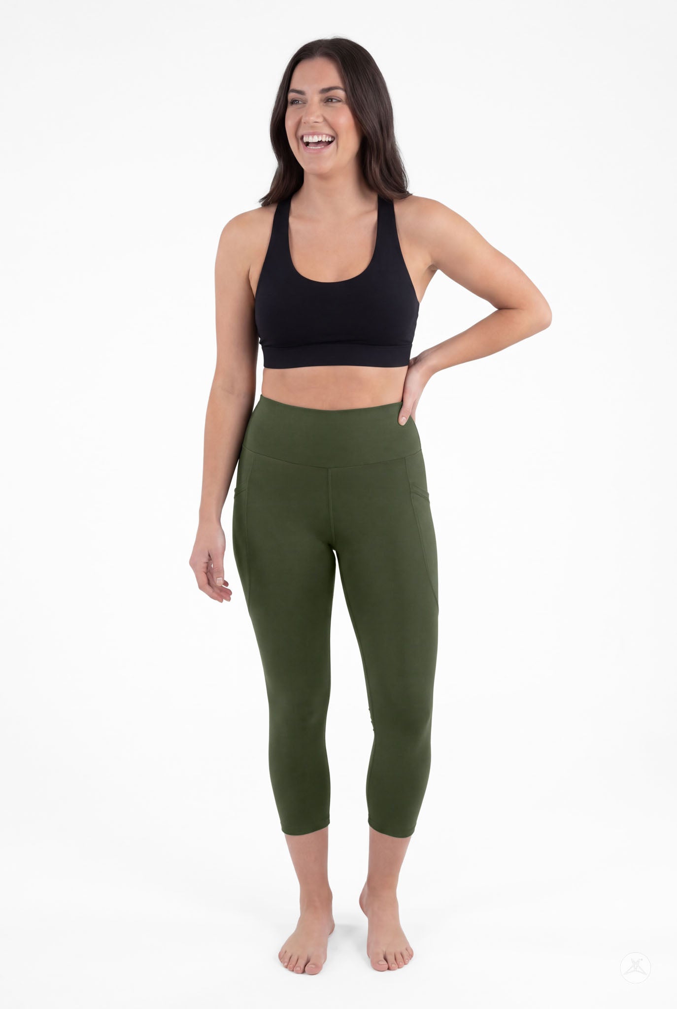 Smiling woman barefoot wearing SweetLegs Cedar High-Waisted Pocket Crops in green with black sports bra standing relaxed